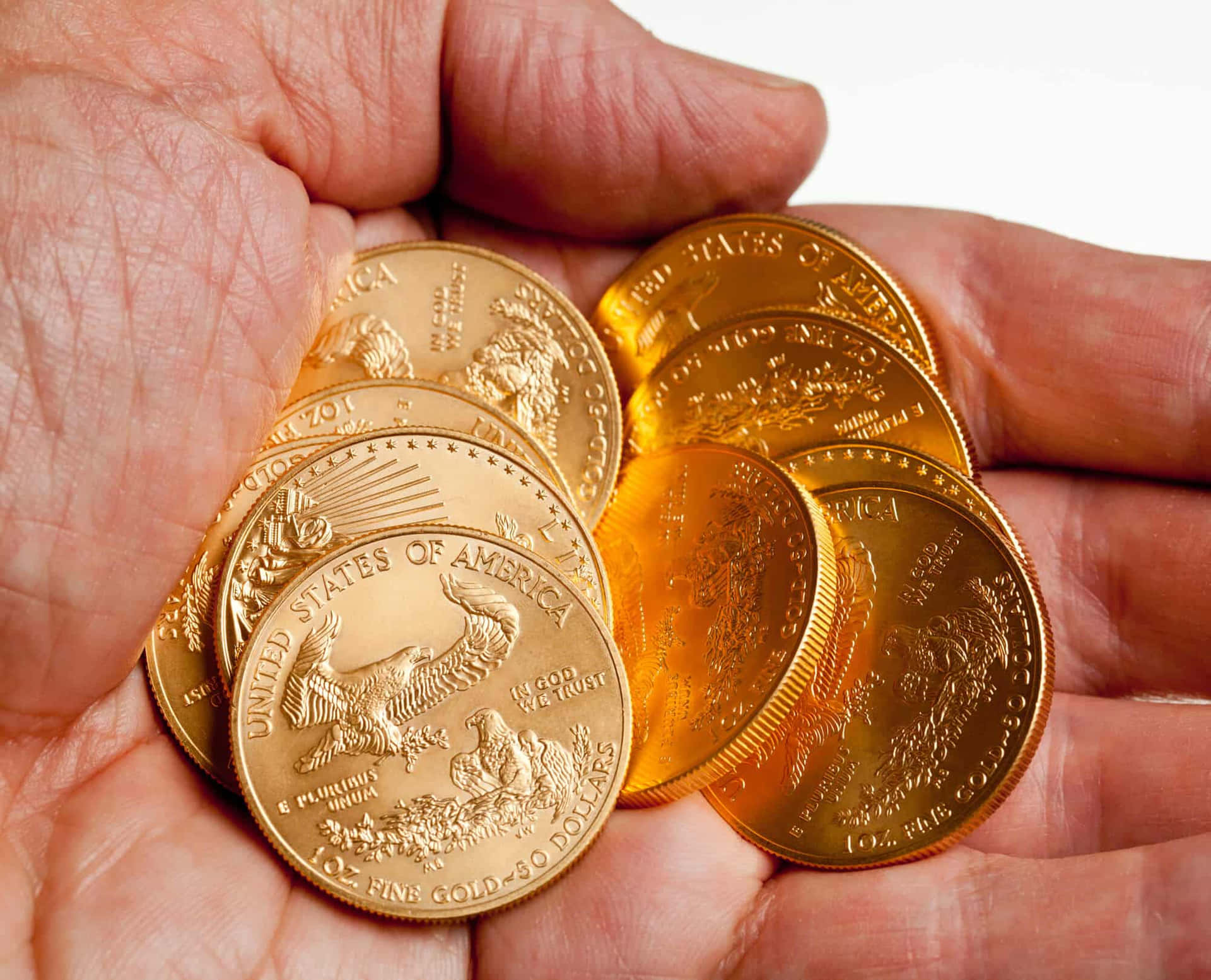 金之純粹之美 壁紙 — 一隻手捧著幾枚閃閃發光的美國鷹揚金幣，背景是明亮的白色。