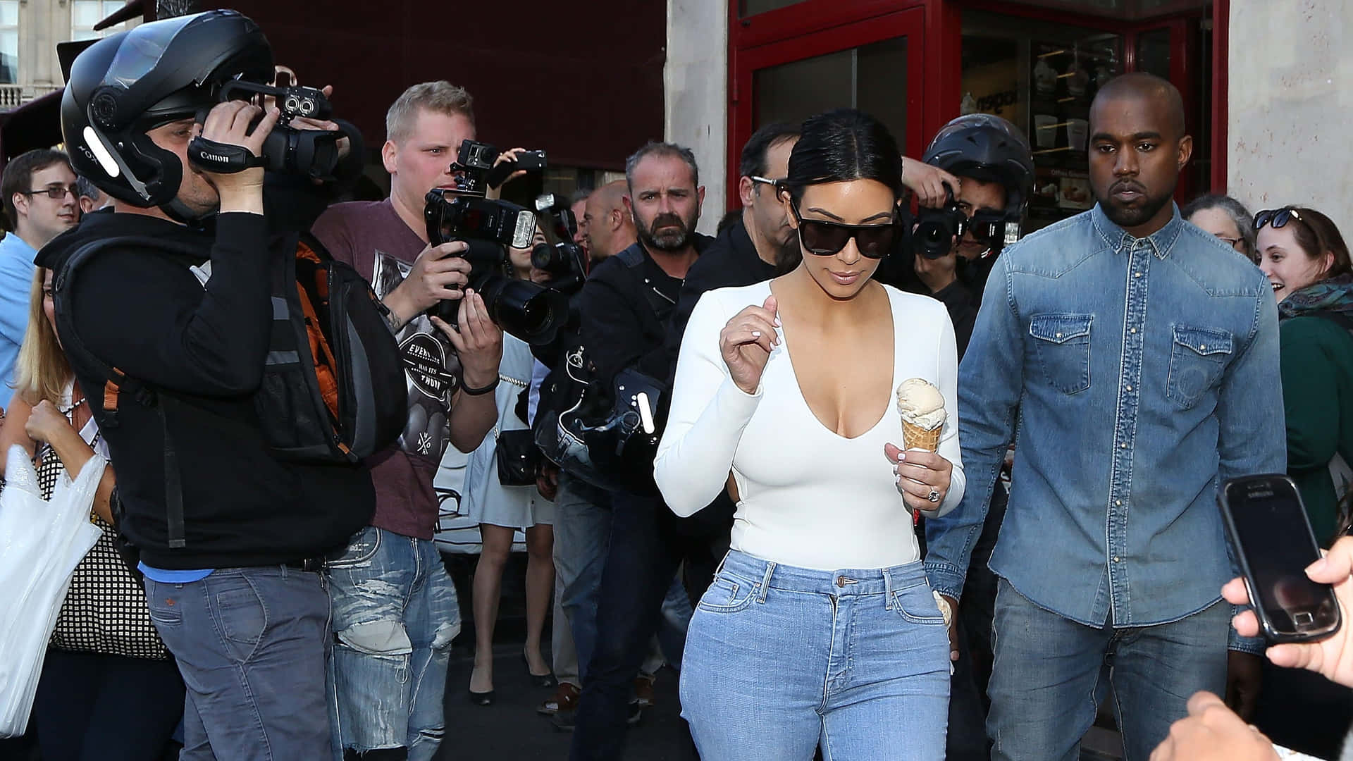 Kim Kardashian 和 Kanye West 在戶外吃雪糕，被攝影師包圍。