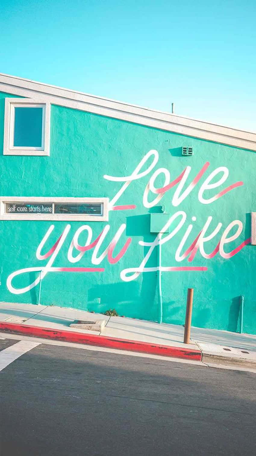 藍綠色建築物，帶有粉紅色和白色的「Love you like」塗鴉壁畫。