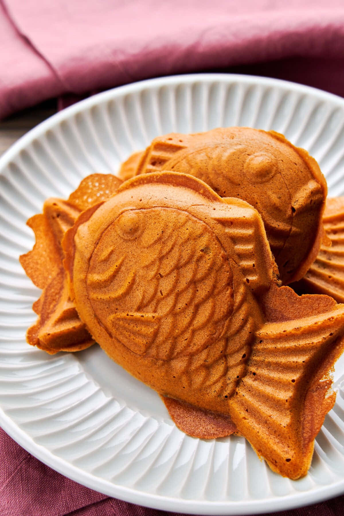 Japanese Sweets 桌布 壁紙 — 金啡色魚形窩夫，帶有細緻鱗片紋理，堆疊在白色坑紋碟上，襯以柔軟粉紅色布料。