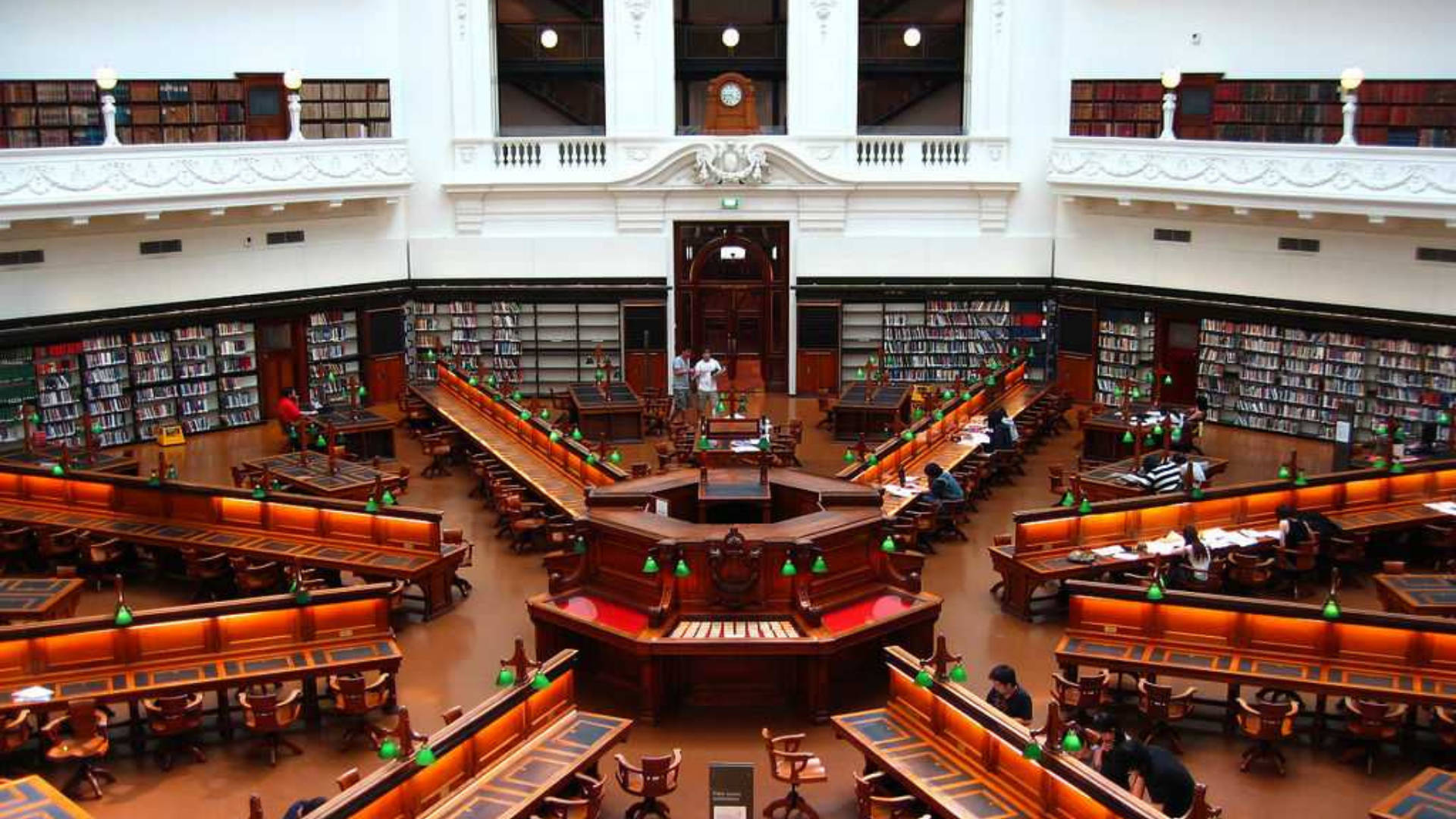 金奈康內馬拉圖書館 壁紙 — 宏偉的圖書館，擁有高聳的天花板、華麗的陽台和溫暖燈光下的木製閱讀桌。