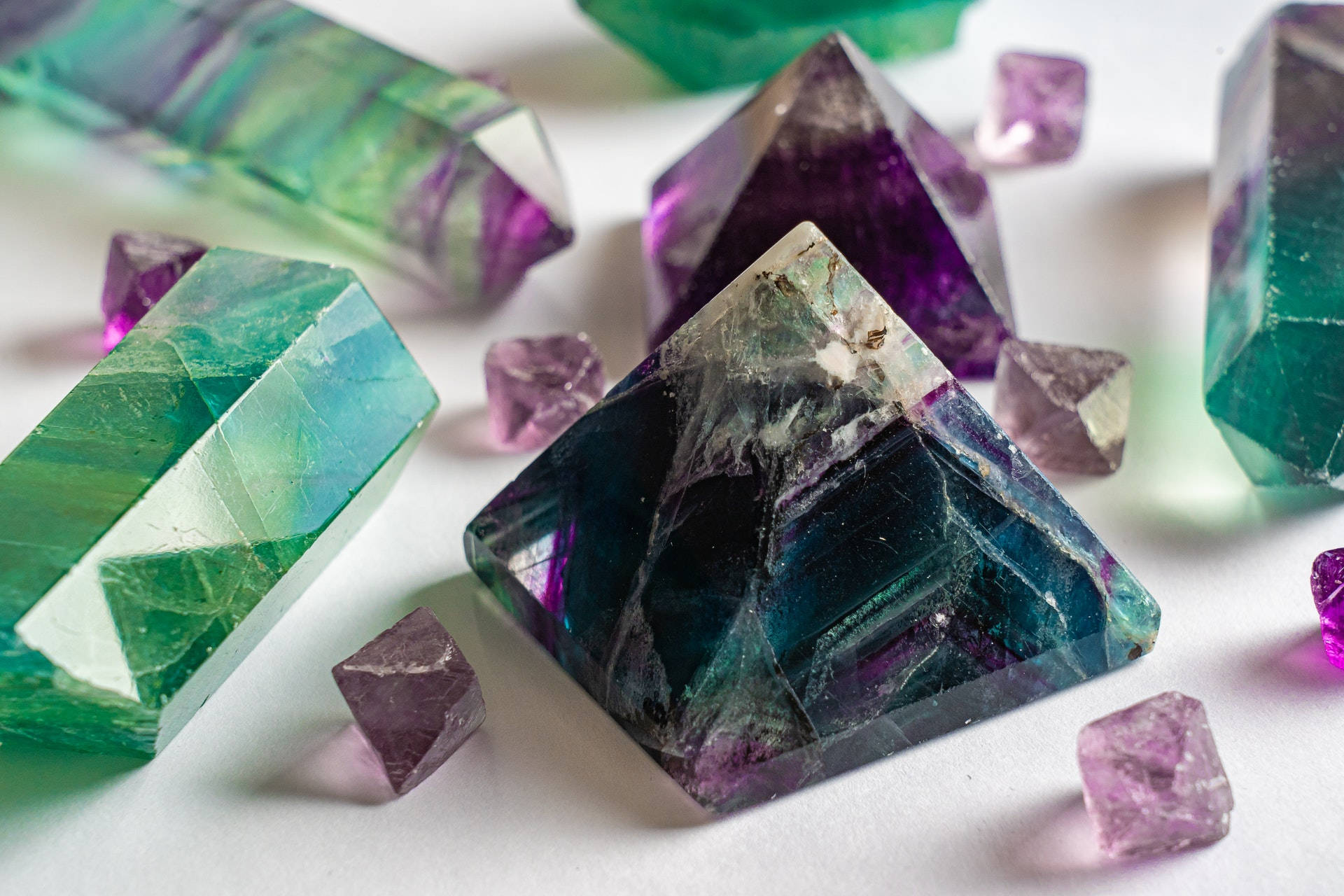 金字塔切割紫水晶 壁紙 — 充滿活力的綠色和紫色螢石晶體，帶有銳利的幾何切面，在白色表面上柔和光線下閃耀。