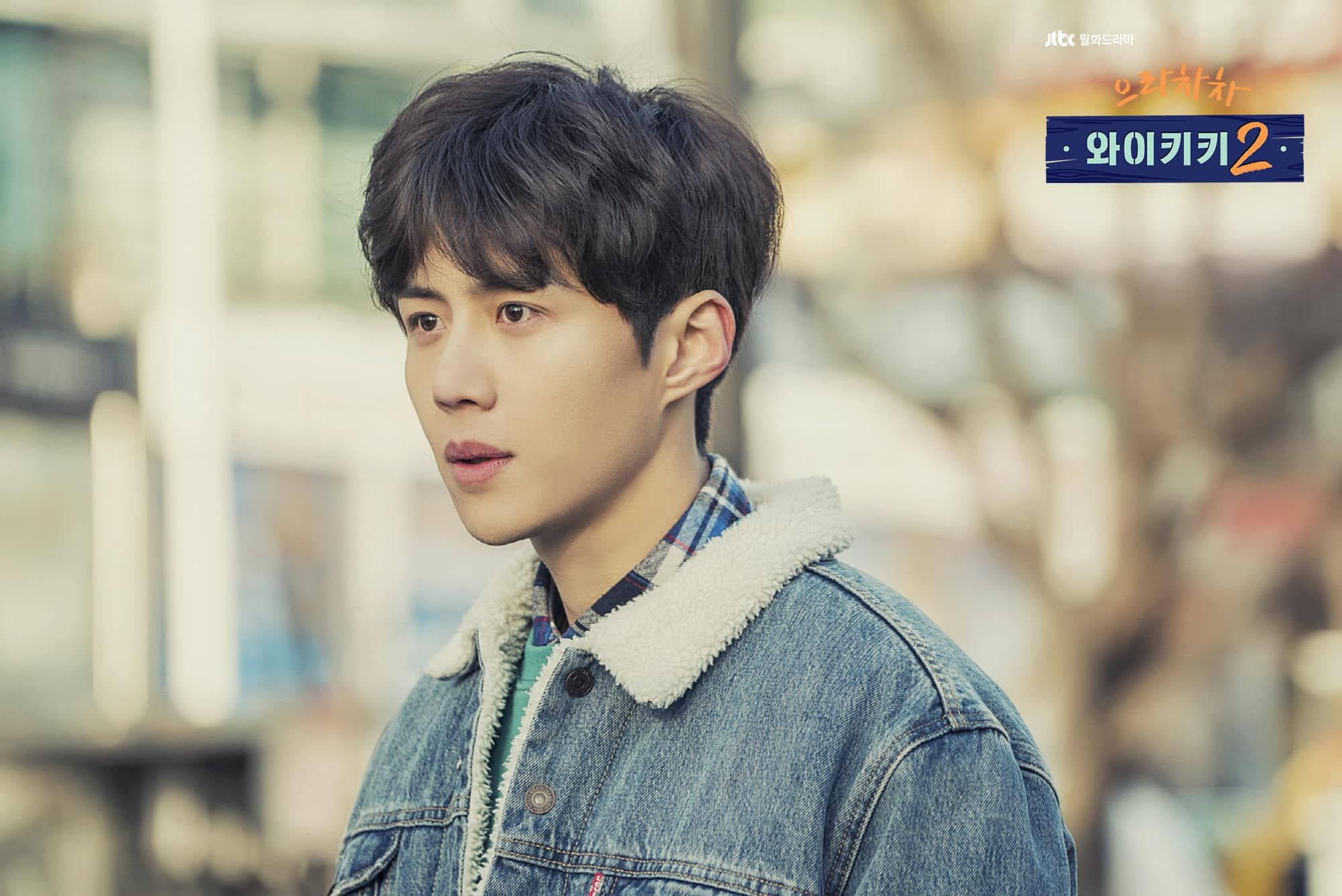 金宣虎《Waikiki 2》劇照 壁紙 — 一位身穿絨毛領牛仔外套的年輕男子，在模糊的城市背景下若有所思地望著戶外。