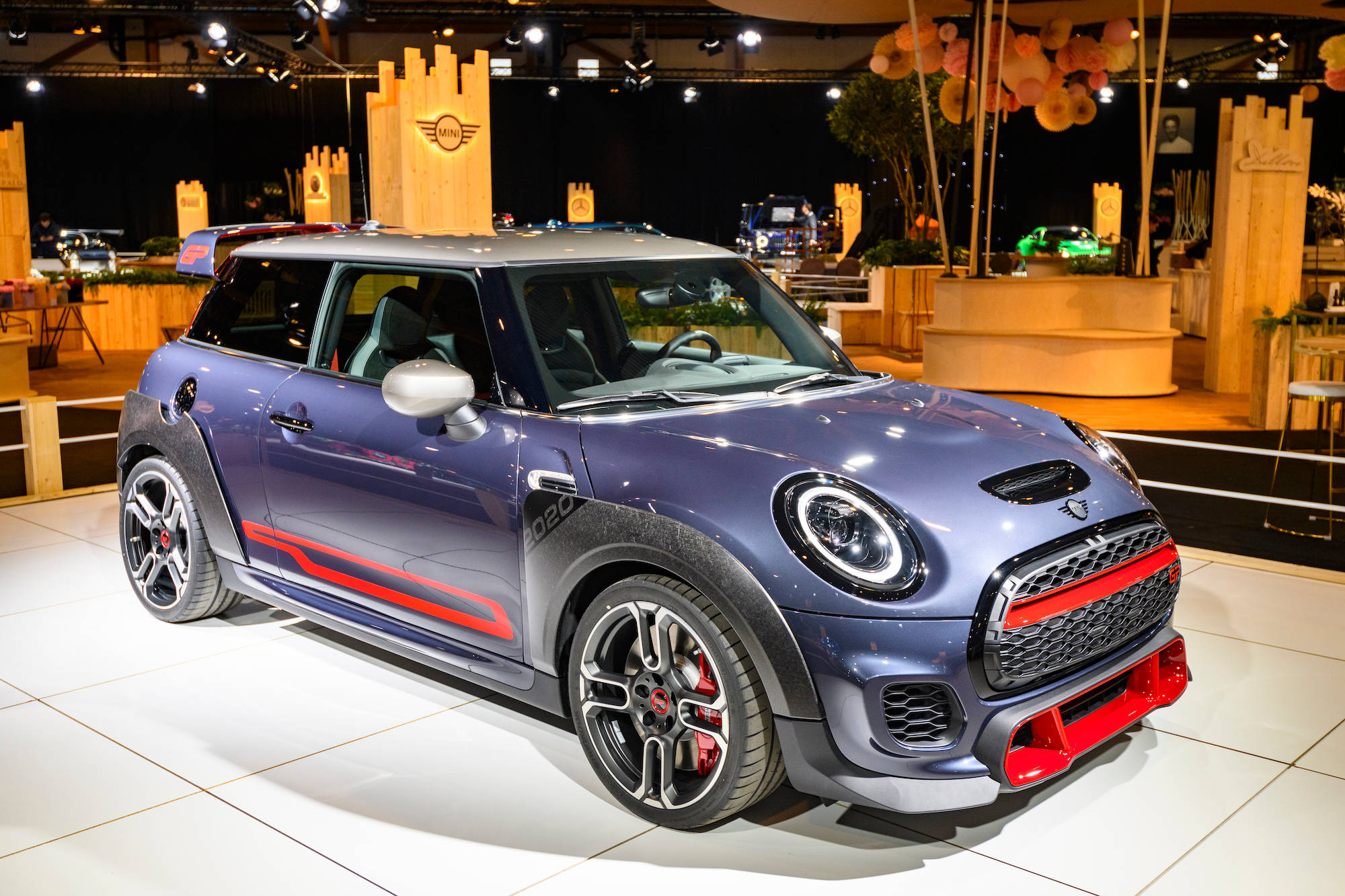金室中央的紫紅色Mini車 壁紙 — 一輛時尚的金屬藍色MINI Cooper JCW，帶有紅色點綴，在白色瓷磚地板上閃耀著明亮的展覽燈光。