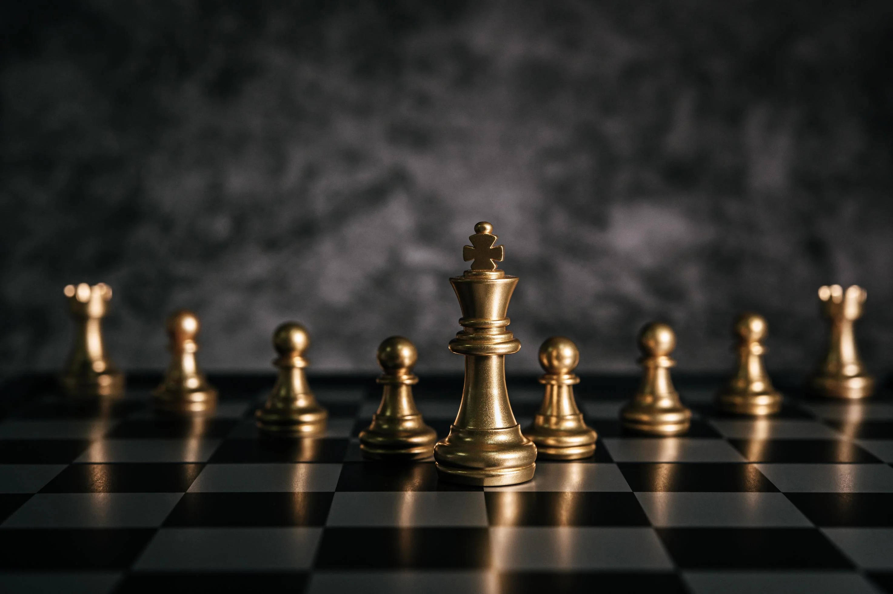 金屬棋子 黑色棋盤 壁紙 — 金色國際象棋棋子擺放在棋盤上，背景是煙霧瀰漫的黑暗環境，帶有戲劇性的燈光效果。