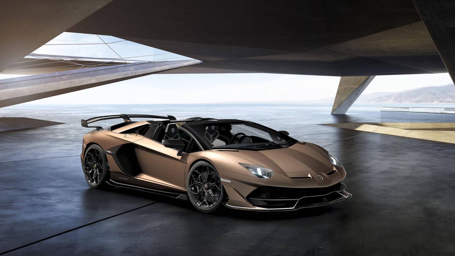 青銅色林寶堅尼Aventador SVJ Roadster停放在海邊的現代混凝土建築下。