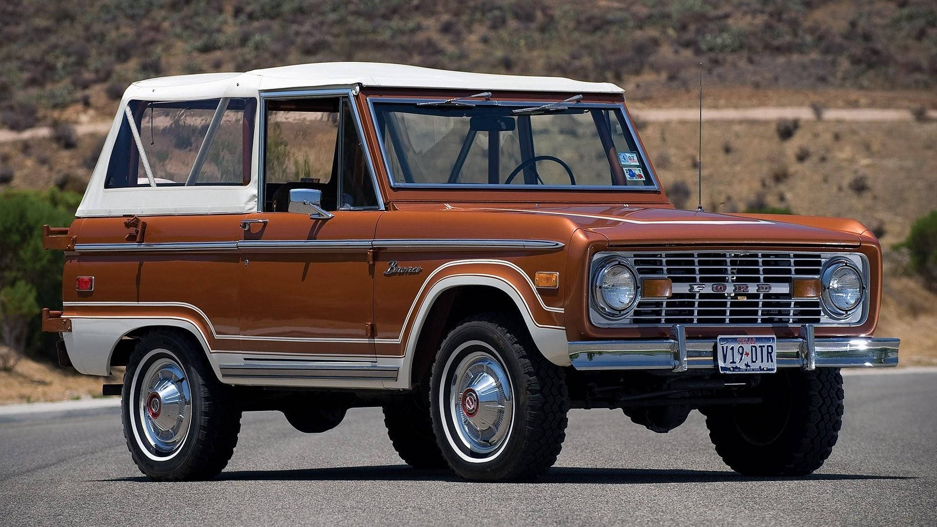 金屬橙色塗裝的福特 Bronco 壁紙 — 一輛復古橙色和白色的福特Bronco，帶有鍍鉻裝飾，停在沙漠公路上，陽光普照。