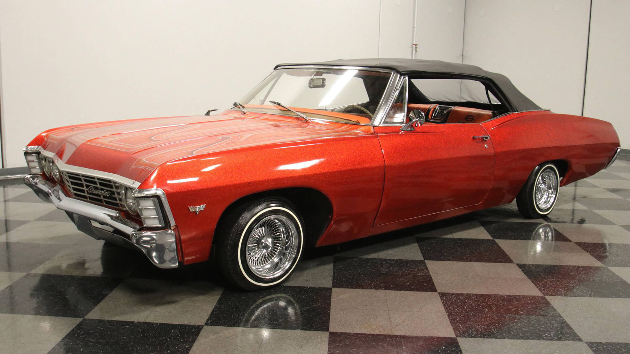 金屬橙色雪佛蘭Impala 1967 壁紙 — 一輛光澤的紅色經典敞篷車，帶有鍍鉻細節和白色輪胎，停在黑白棋盤格地板上。