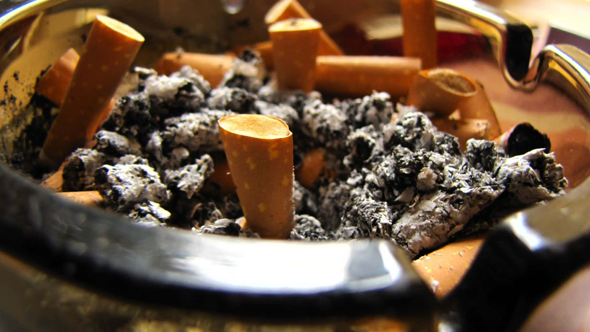 吸煙 桌布 壁紙 — 金屬煙灰缸在溫暖燈光下裝滿煙頭和煙灰的特寫。