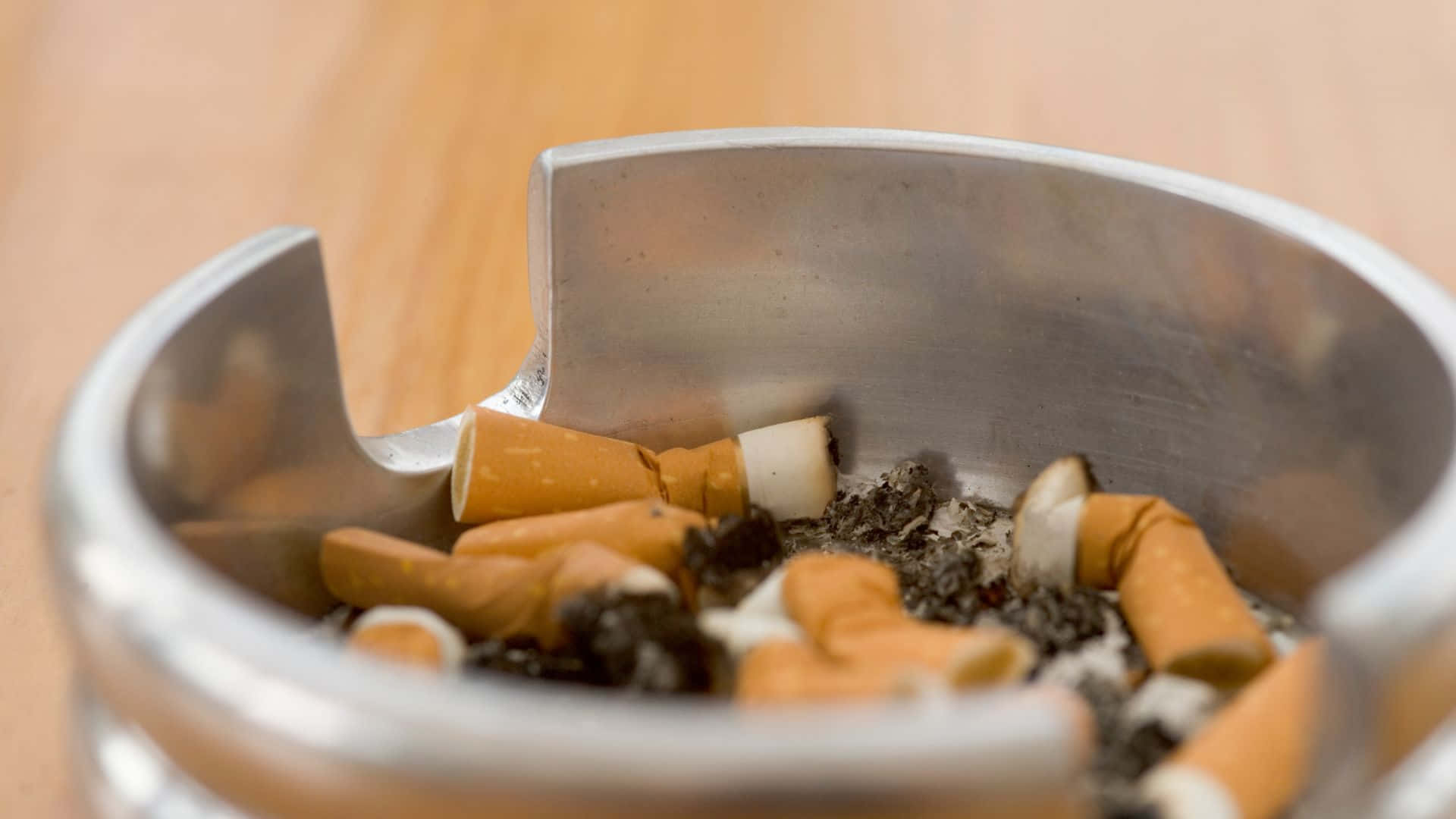 吸煙 桌布 壁紙 — 金屬煙灰缸裝滿煙頭和煙灰在木質表面上的特寫。