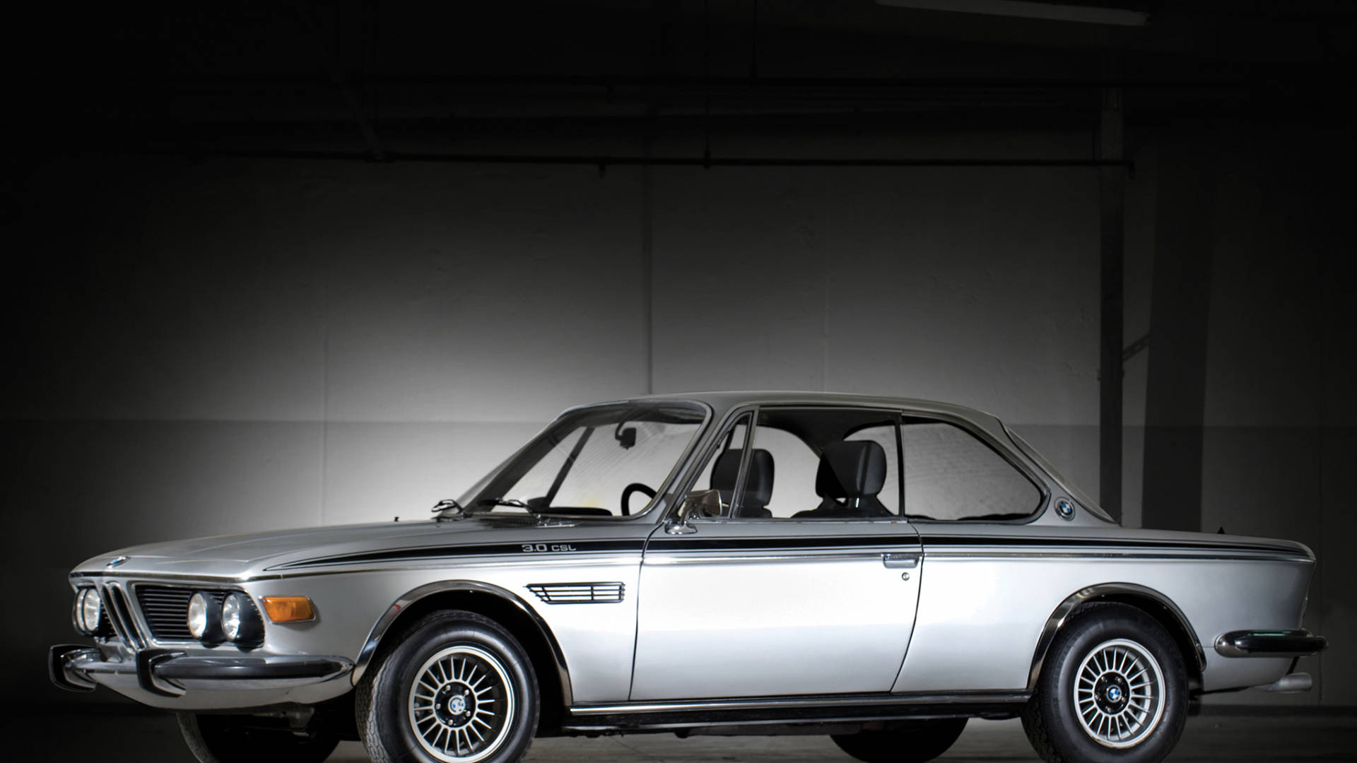 在黑暗工作室中，聚光燈下的銀色經典BMW 3.0 CSL跑車。