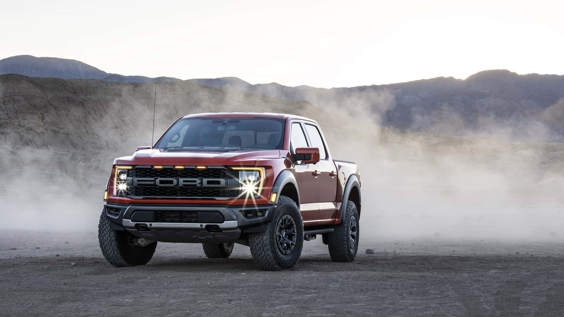 紅色福特 F-150 Raptor 貨車在日出時分駛過沙漠，揚起塵雲。
