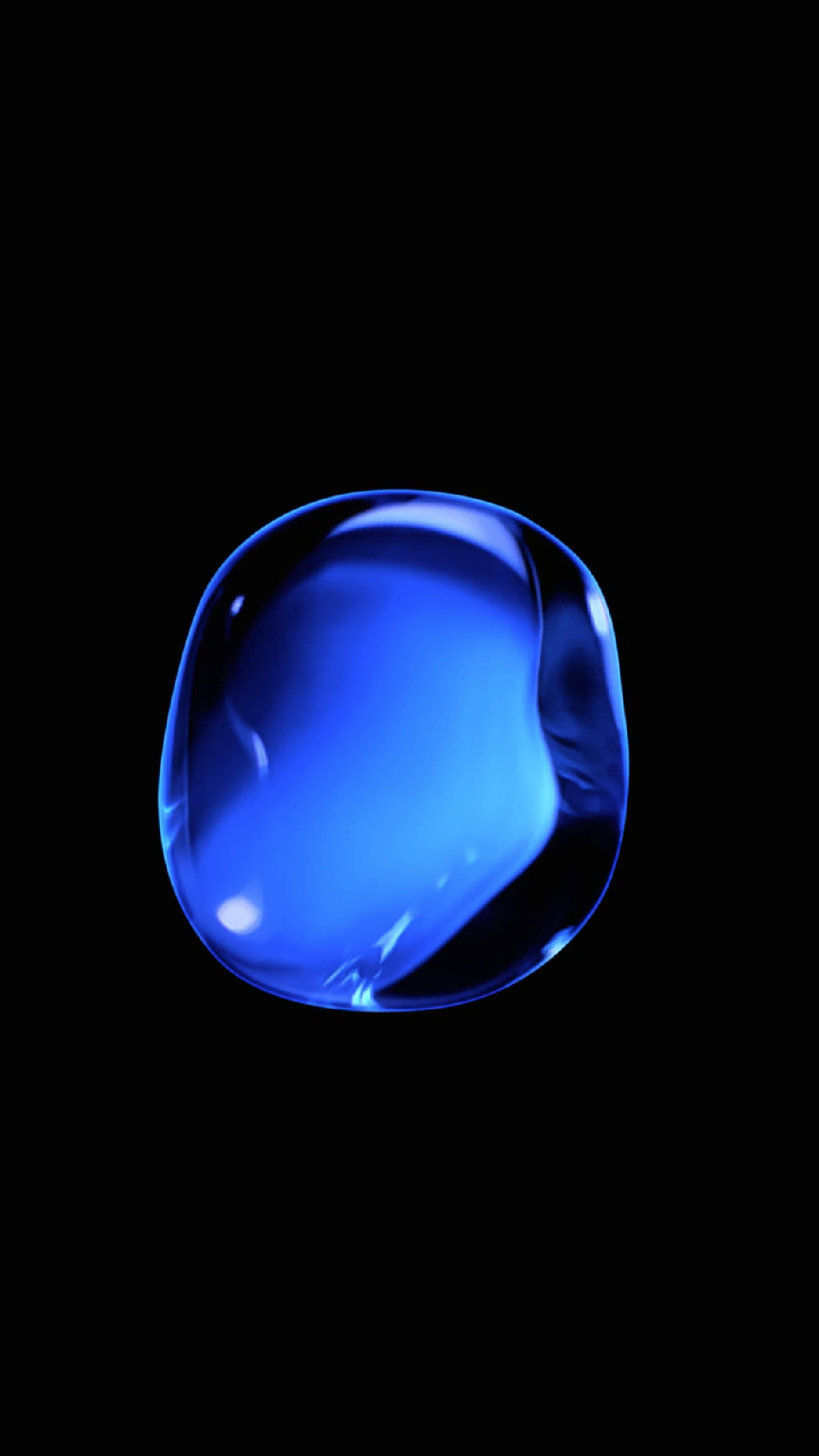 金屬藍色液體 iPhone 活動壁紙 壁紙 — 一顆發光的藍色水滴漂浮在純黑背景上，內部反射閃耀。
