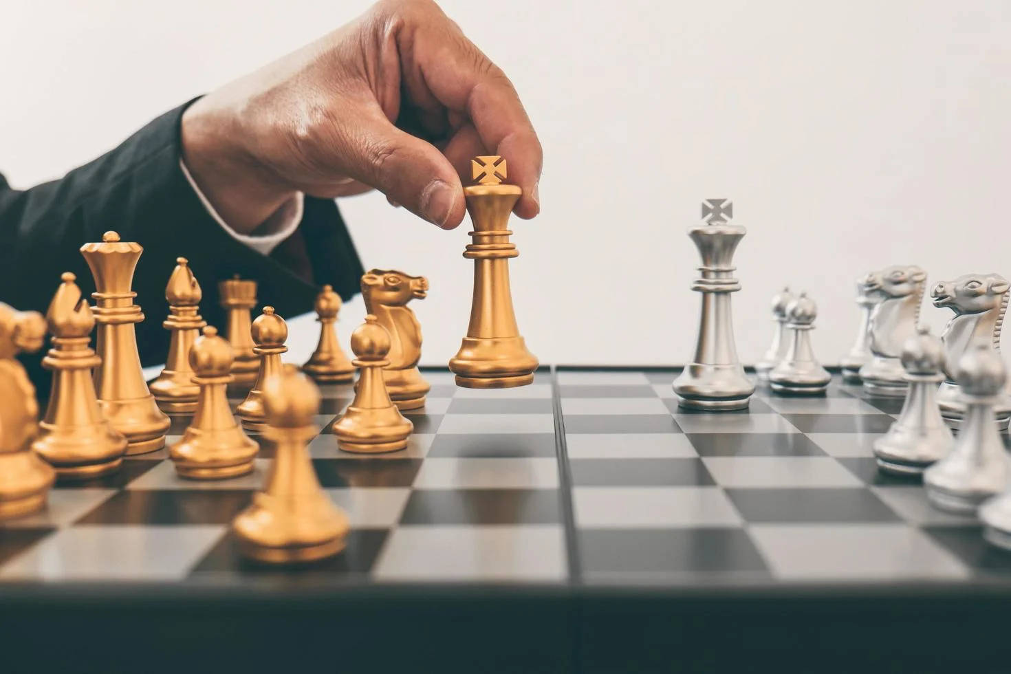 金屬金棋王：尊貴與戰略的化身 壁紙 — 一隻穿著西裝的手在棋盤上移動金色國王棋子，面對銀色棋子。