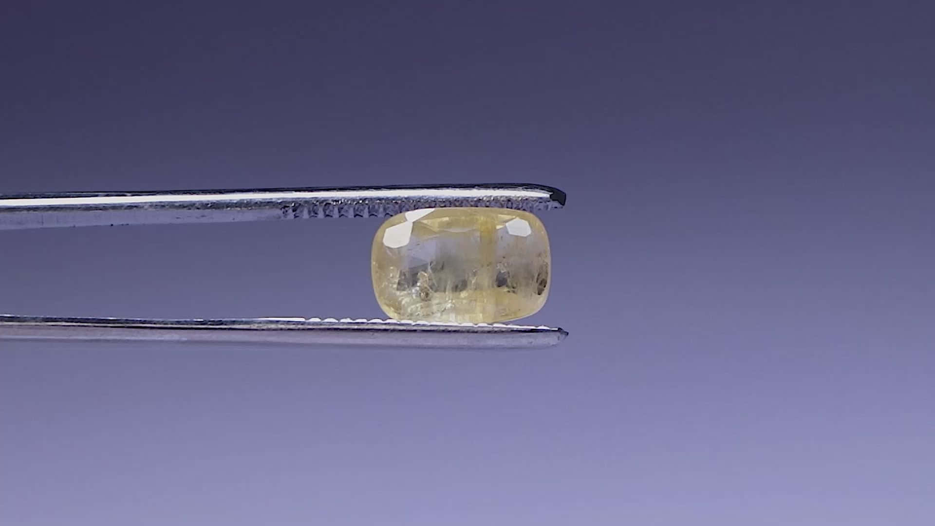 Yellow Sapphire 桌布 壁紙 — 金屬鑷子夾住一顆淡黃色枕形切割寶石，背景為漸變紫色。
