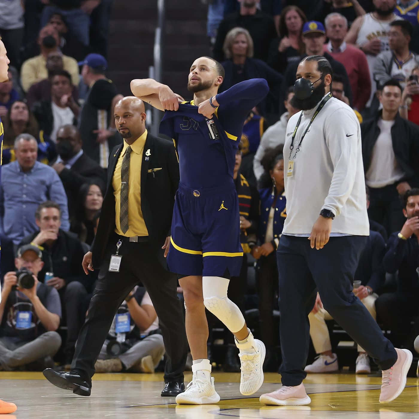 steph curry 桌布 壁紙 — 金州勇士隊球員史提芬居里在比賽期間，在拋光硬木球場上伸展，周圍有觀眾和工作人員。