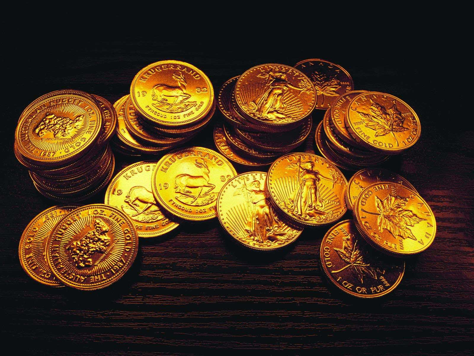 金幣包裝巧克力 壁紙 — 一堆閃閃發光的金幣，帶有精細雕刻，放在溫暖燈光下的深色木質表面上。