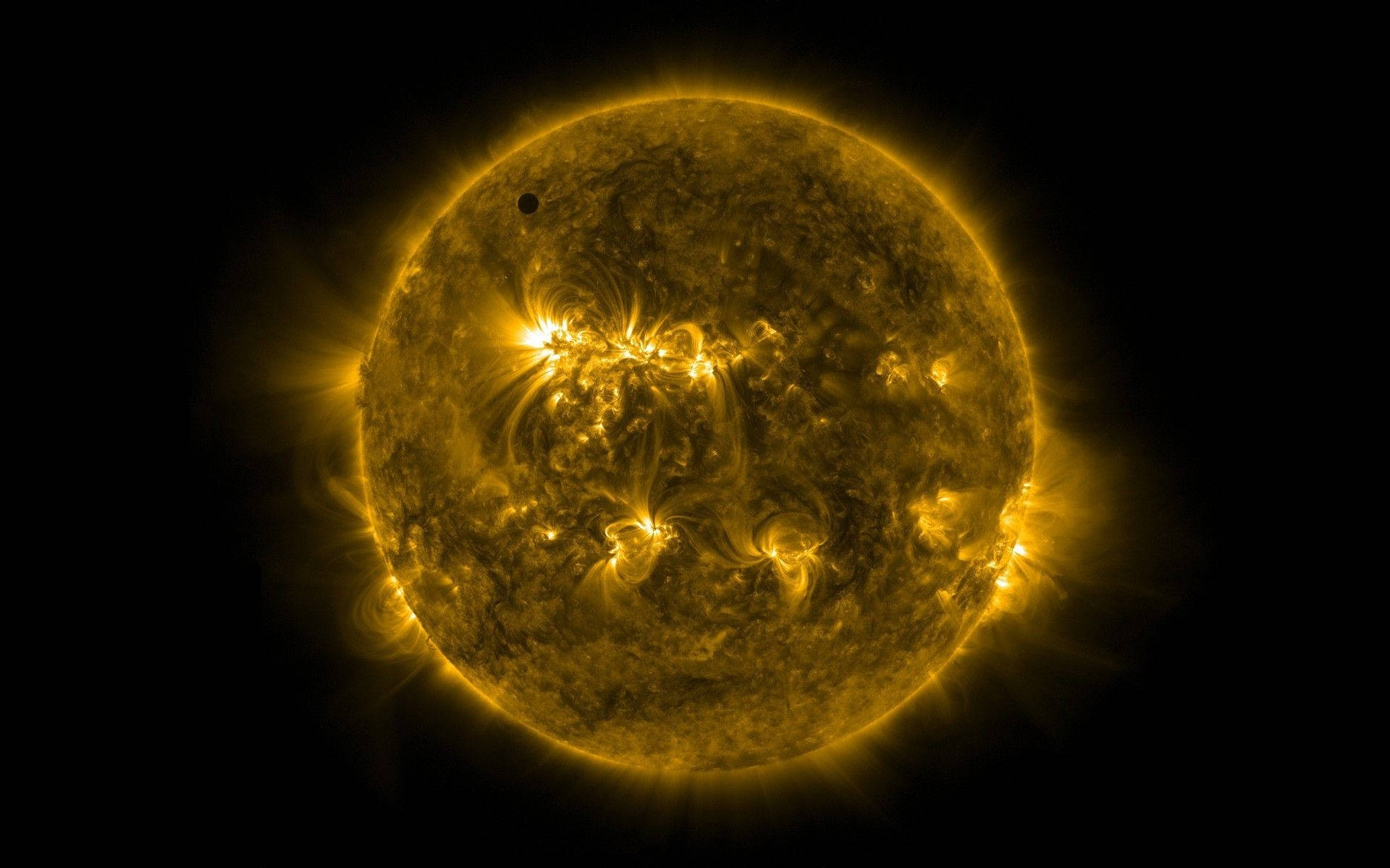 金星發出黃色閃焰 壁紙 — 一顆熾熱的金色太陽，帶有旋轉的太陽耀斑和一顆在黑色虛空前經過的小型暗色行星。