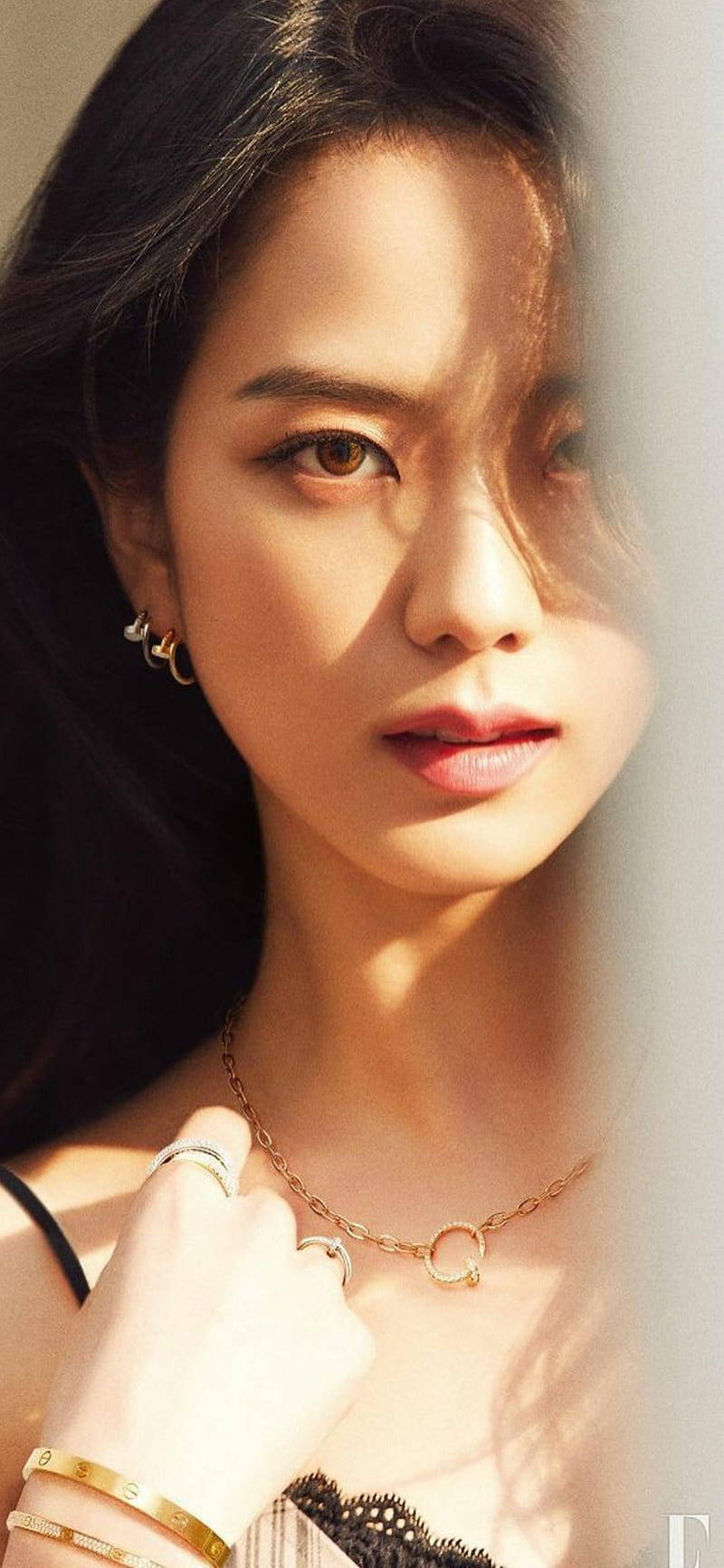 女性在柔和陽光下佩戴金色珠寶和黑色蕾絲上衣。