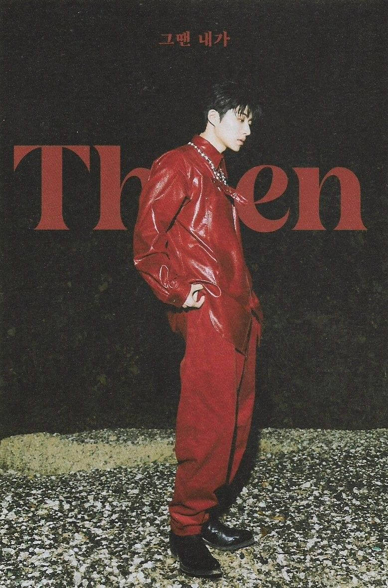 金漢彬《THEN》 壁紙 — 一名身穿亮面紅色連身褲的年輕男子自信地站在帶有粗體紅色字體的深色紋理牆壁前。