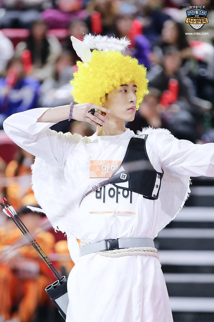 金漢彬愛神造型 壁紙 — 一名身穿白色服裝、戴著黃色假髮和狐狸耳朵的人，在電視轉播的射箭比賽中瞄準弓箭。