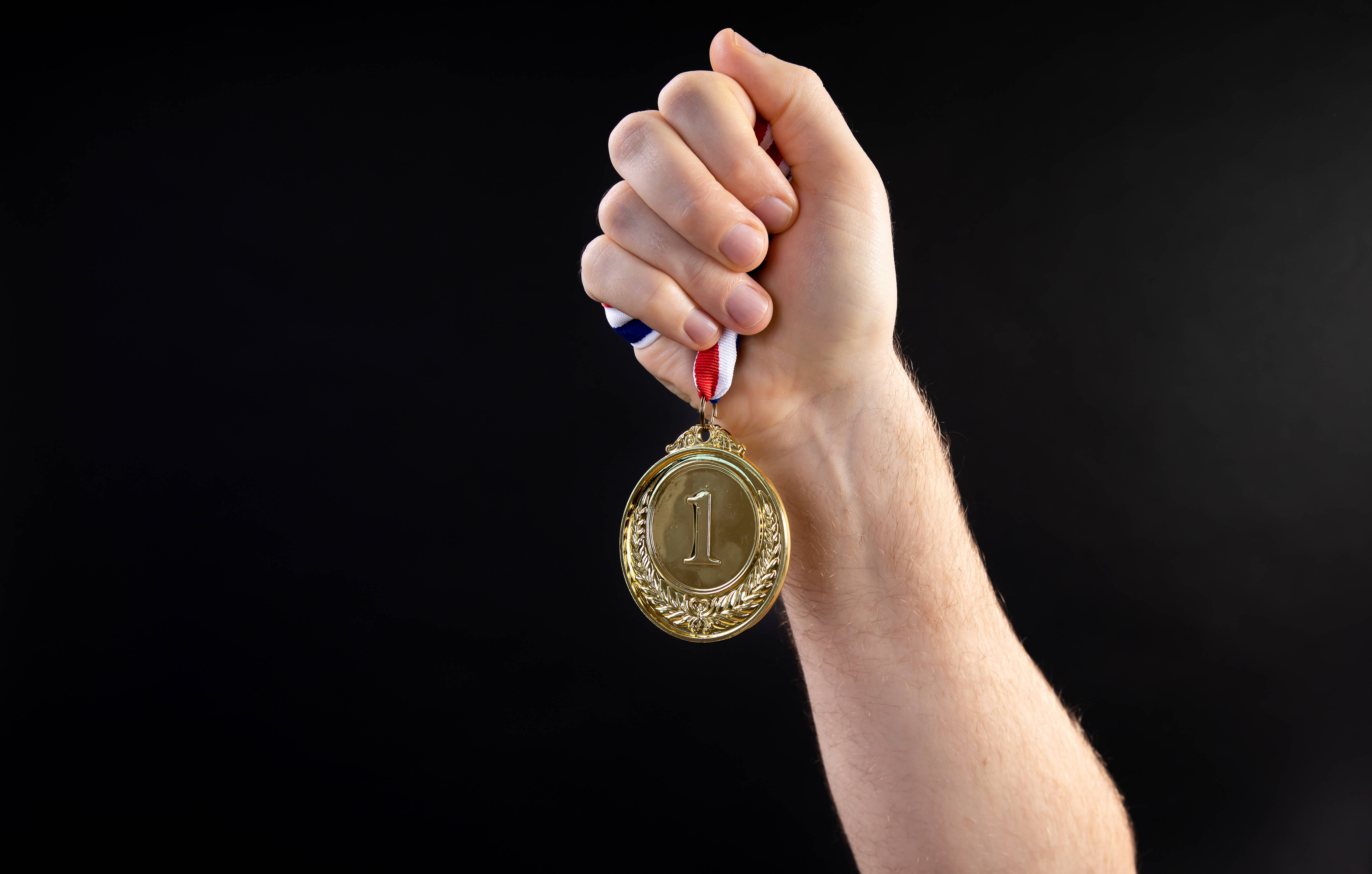金牌勝利 壁紙 — 一隻手自豪地握著一枚金色第一名獎牌，背景是純黑色。