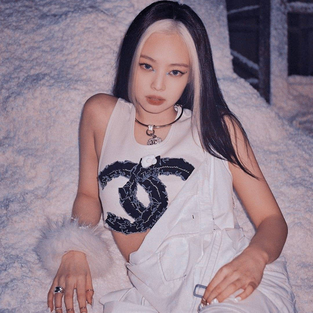 金珍妮穿香奈兒性感短上衣 壁紙 — 一位擁有黑白頭髮的女性，穿著白色 Chanel 套裝，自信地坐在有紋理的灰色背景前。