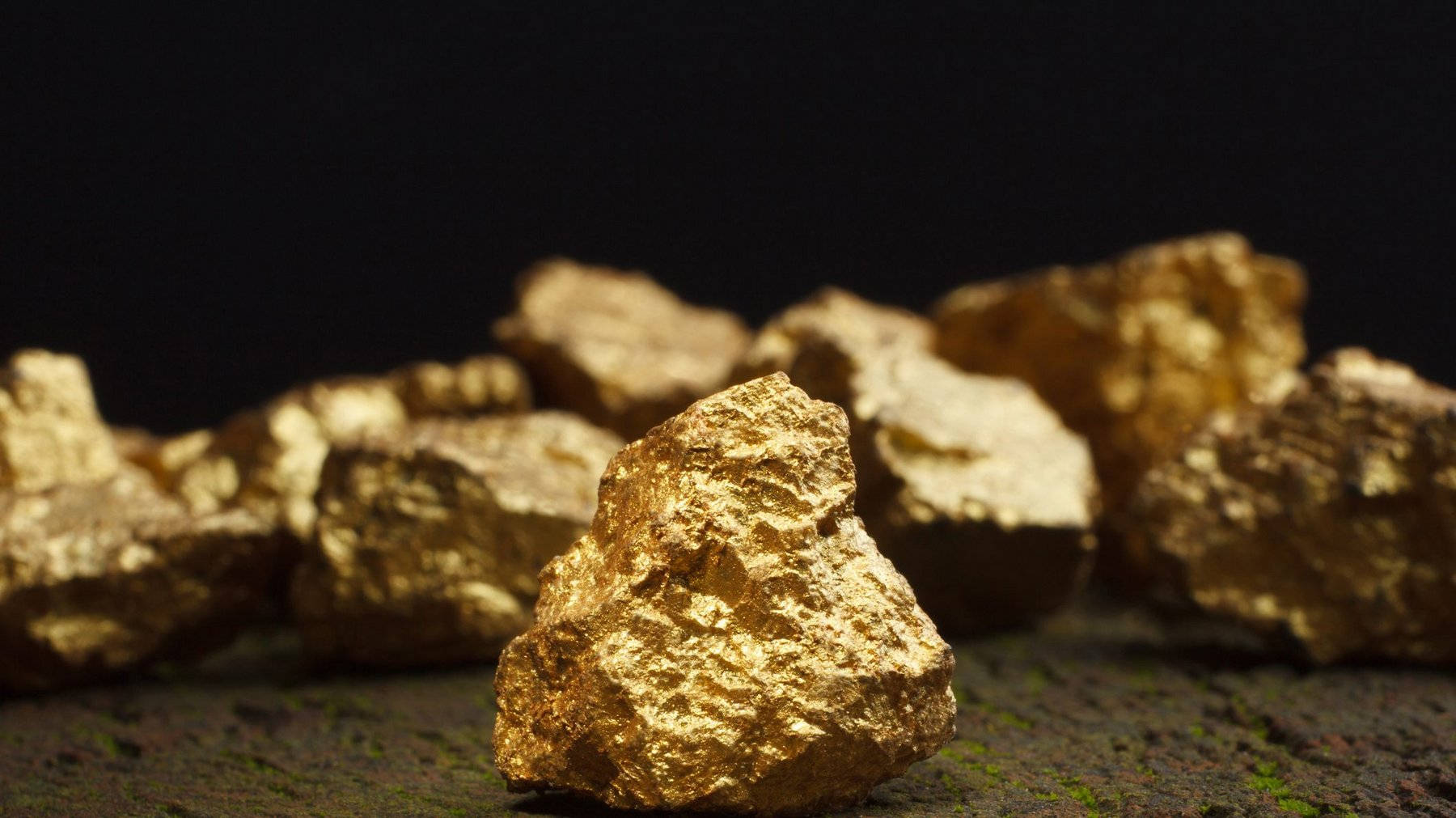 金礦中金塊的美學照片 壁紙 — 閃亮的粗糙金塊在聚焦光線下閃耀，背景為帶有苔蘚表面的深色背景。