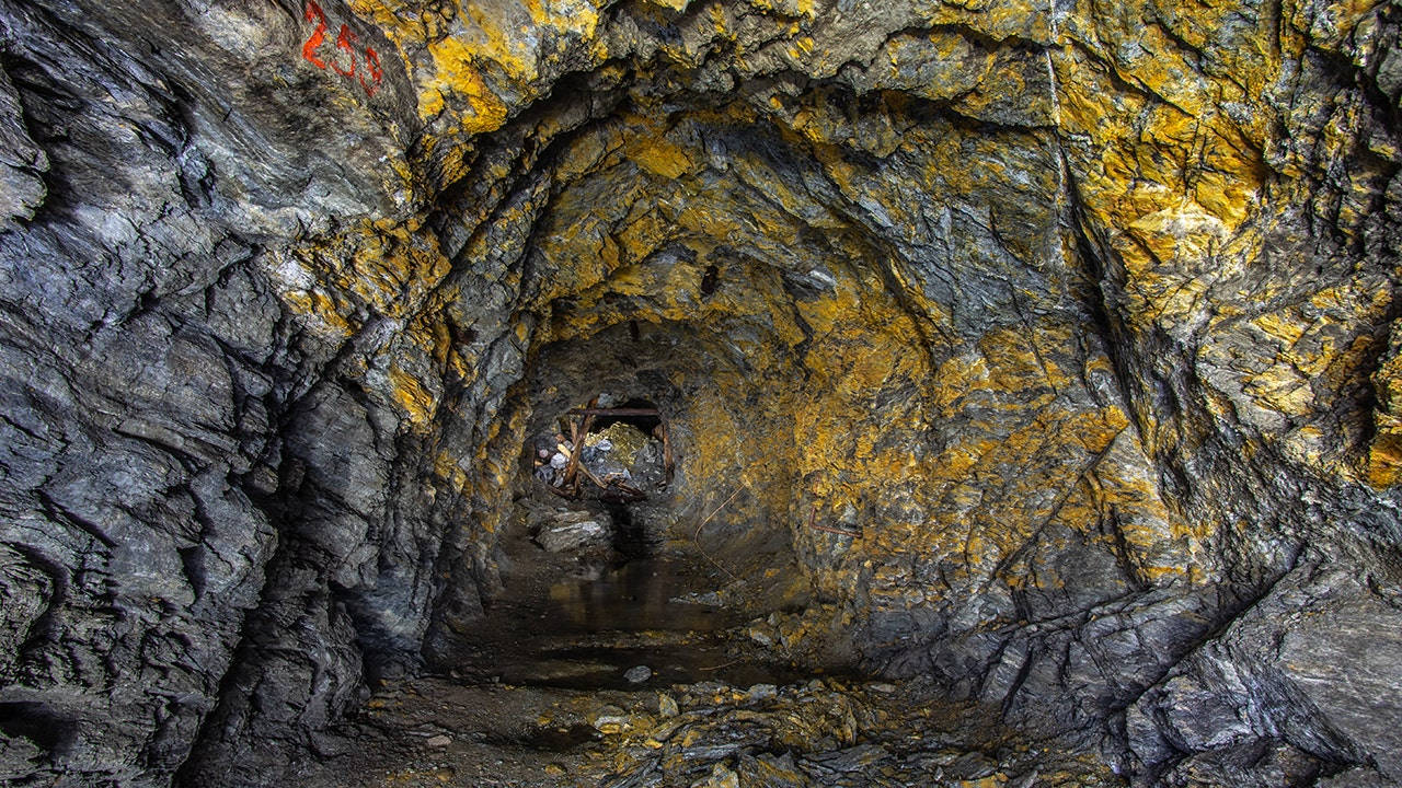 一條狹窄的地下礦井隧道，灰色岩壁上有黃色礦物條紋。