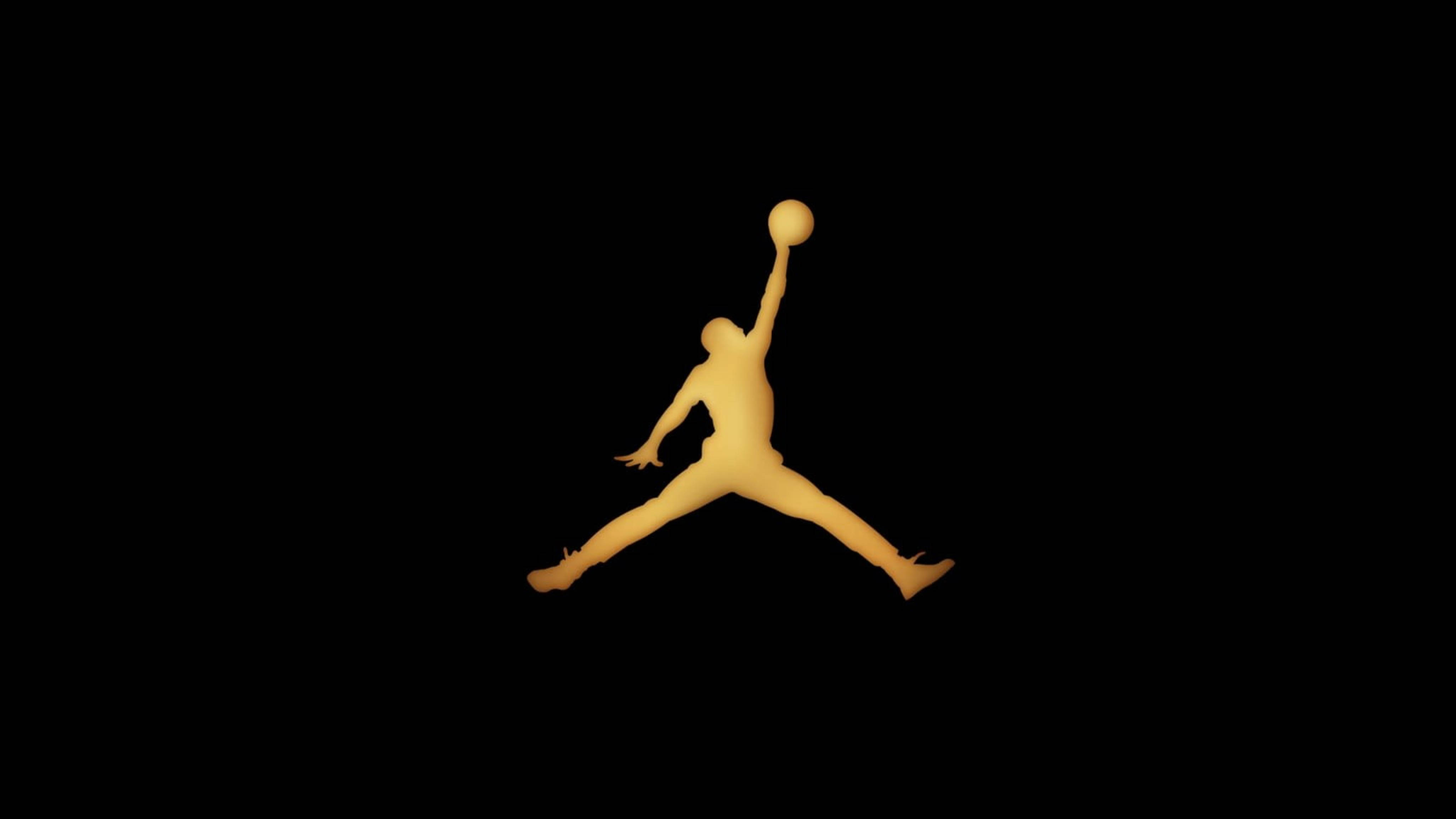 金色 Air Jordan 標誌 壁紙 — 一個發光的金色剪影，描繪一名籃球運動員在半空中灌籃，背景為純黑色。