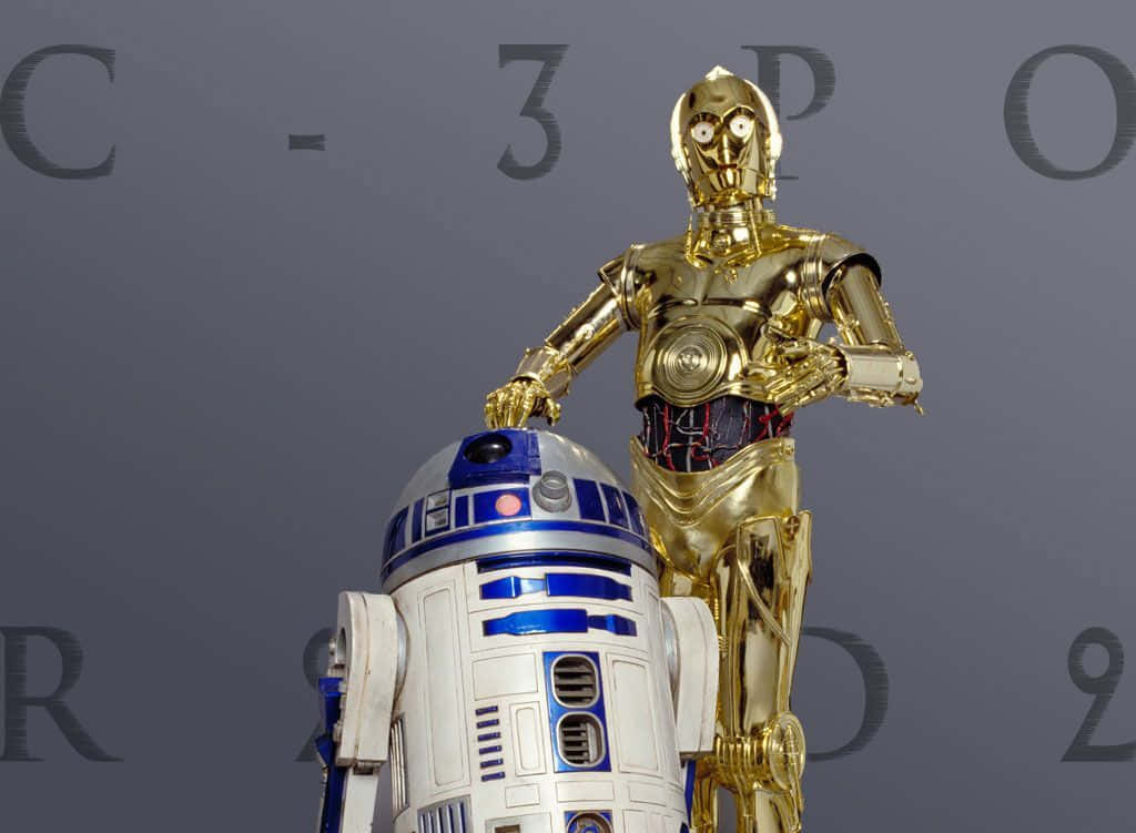 C-3po 桌布 壁紙 — 金色C-3PO和白色藍色R2-D2機械人並排站在帶有模糊文字的灰色背景前。