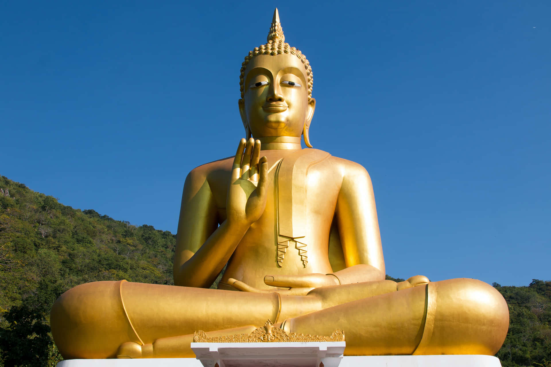 藍天下山坡上蓮花坐姿的金色佛像