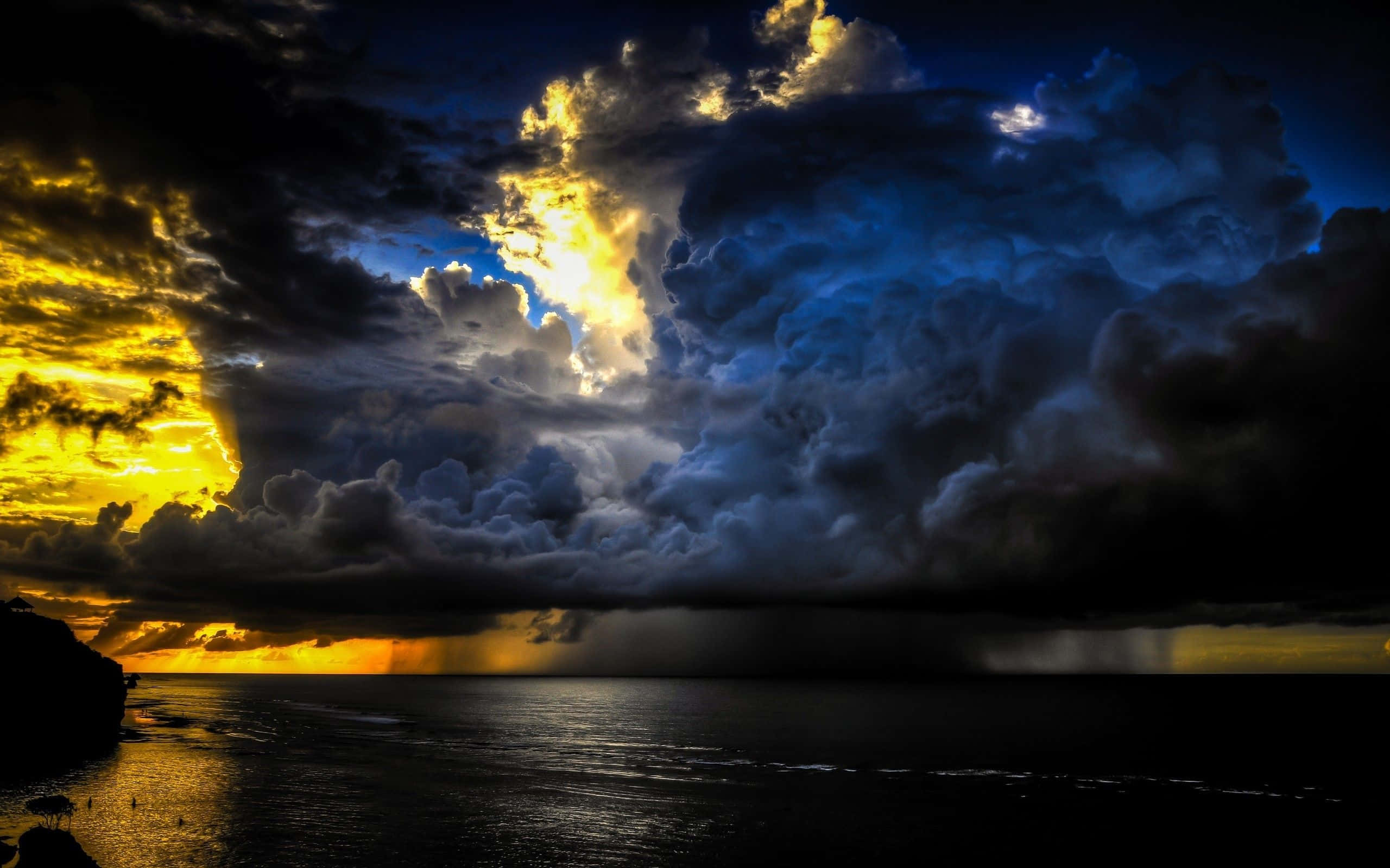 Thunderstorm 桌布 壁紙 — 金色光芒穿透黑暗暴風雲，在平靜海面上投射倒影的戲劇性海上日落。