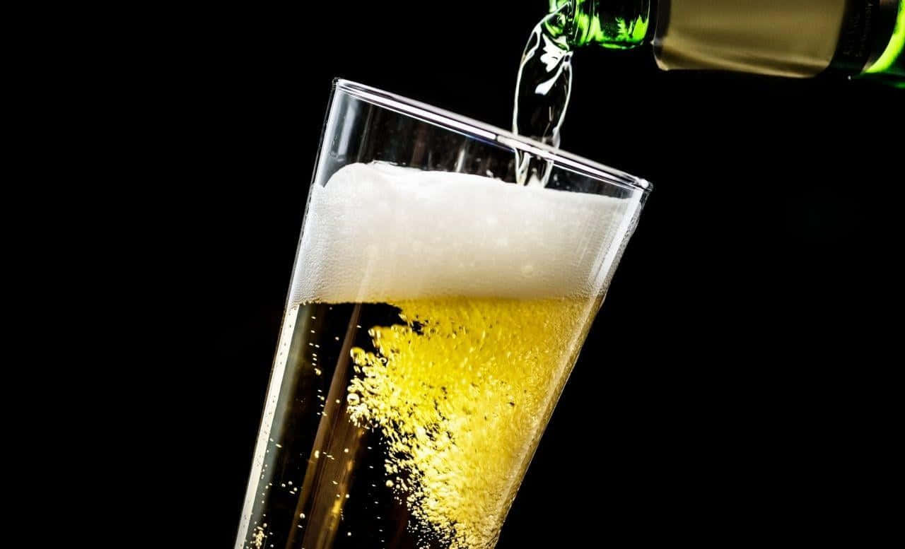 alcohol 桌布 壁紙 — 金色啤酒從綠色瓶子倒入玻璃杯，在黑色背景上形成泡沫豐富的白色泡沫頭。