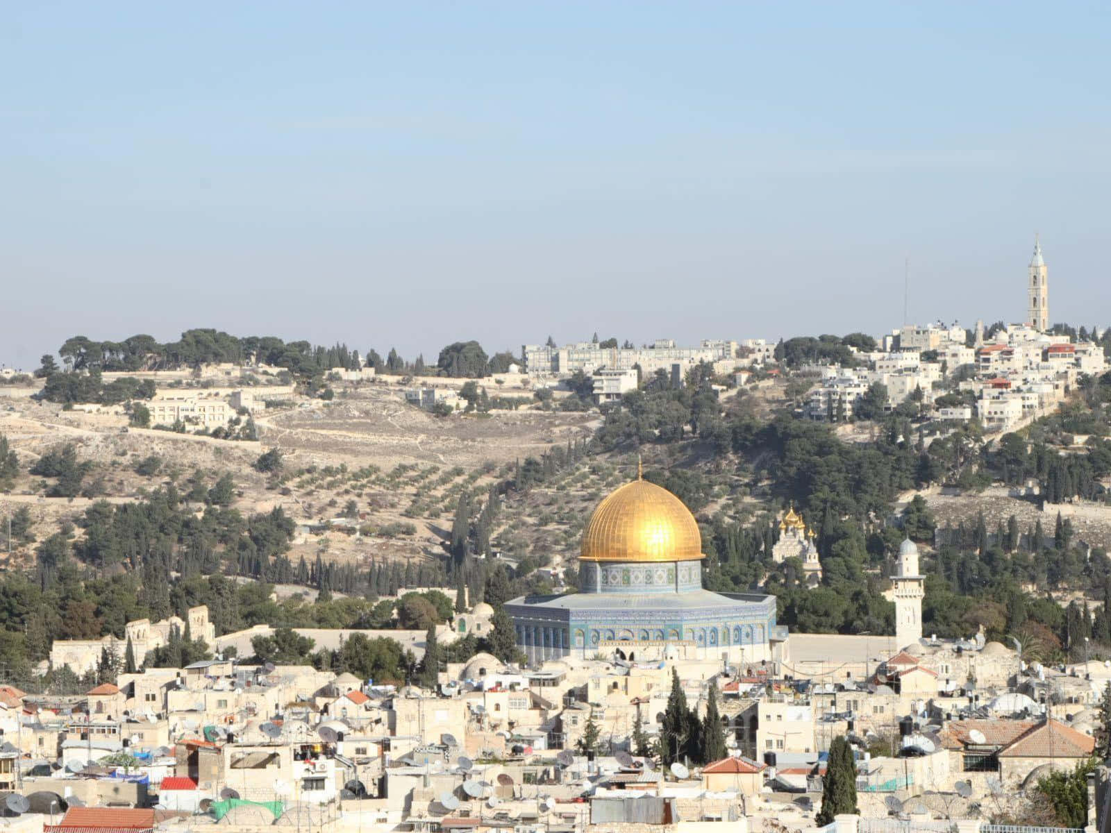 Israel 桌布 壁紙 — 金色圓頂清真寺在藍天白雲下，於被石頭建築和綠樹環繞的山丘頂上閃耀。