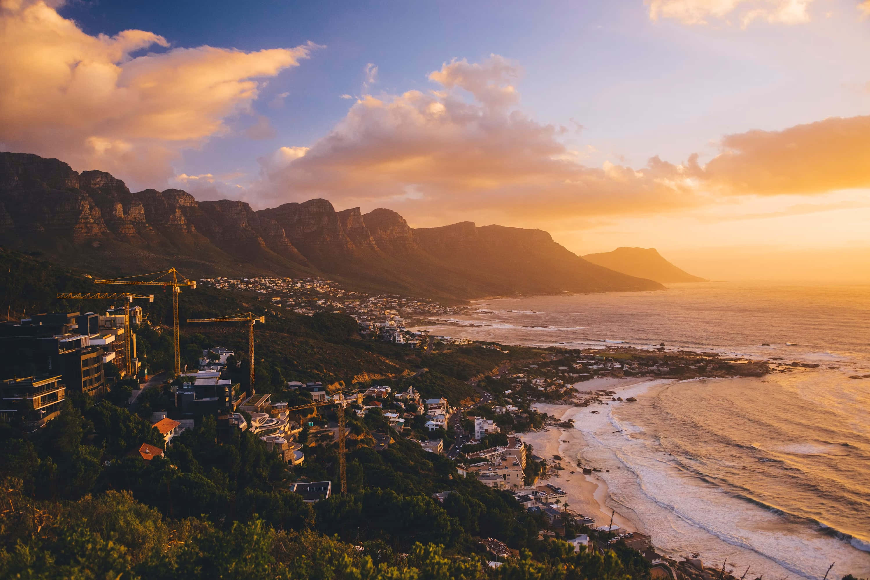 South Africa 桌布 壁紙 — 金色夕陽以溫暖光線沐浴桌山和沿海小鎮，海浪拍打海岸。