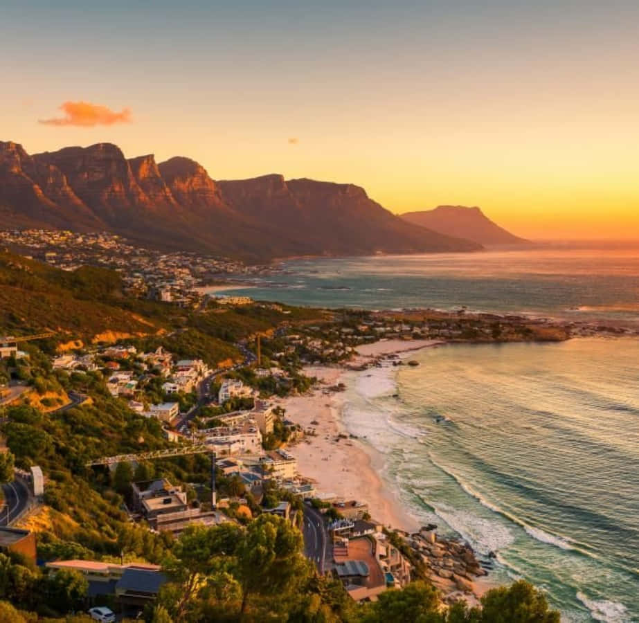 South Africa 桌布 壁紙 — 金色夕陽以溫暖光芒沐浴桌山和沿海小鎮，海浪拍打沙灘。