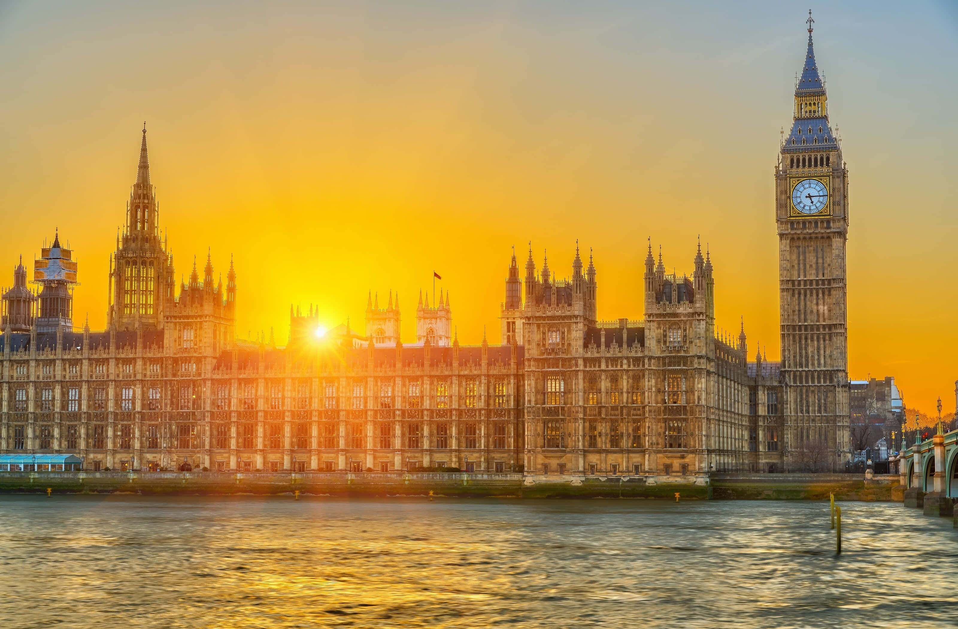 UK 桌布 壁紙 — 金色夕陽以溫暖的光芒沐浴著標誌性的西敏宮和大笨鐘，它們的倒影在泰晤士河上閃爍。