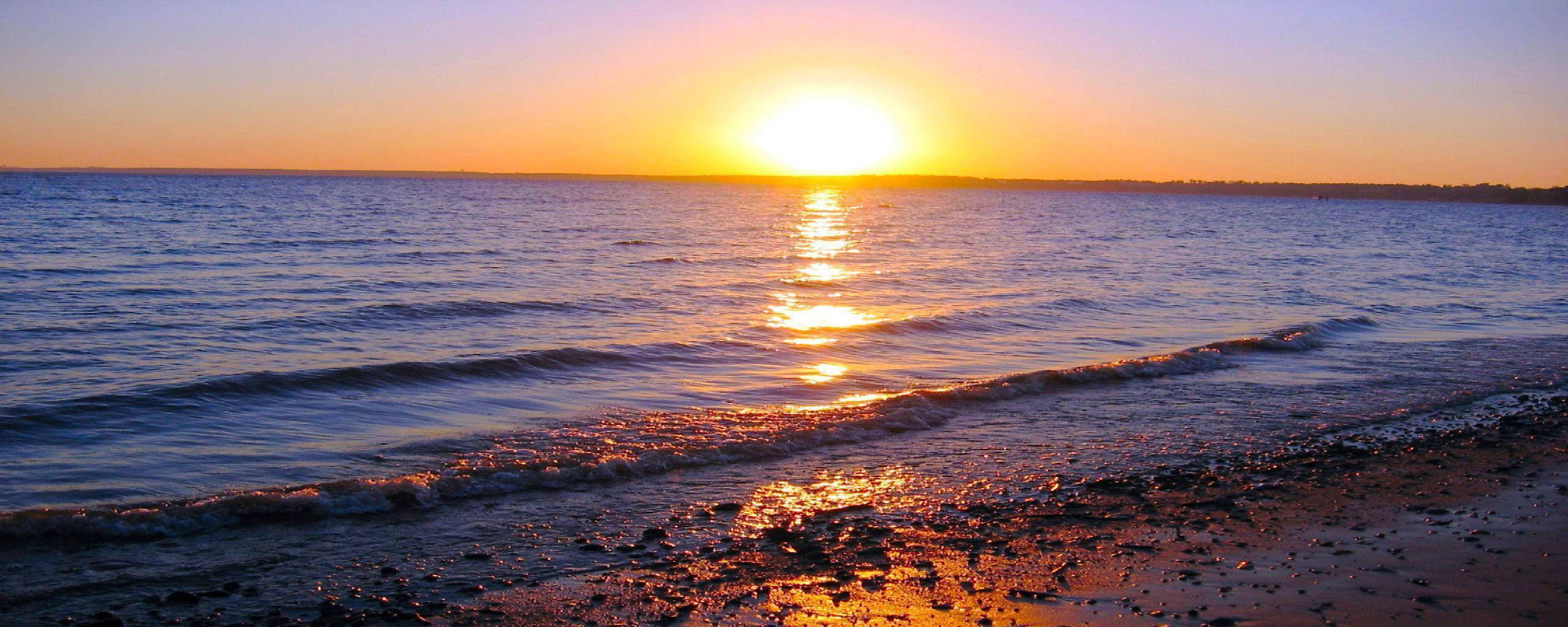 日落 桌布 壁紙 — 金色夕陽在黃昏時分照耀著平靜的海浪沖刷卵石海灘。