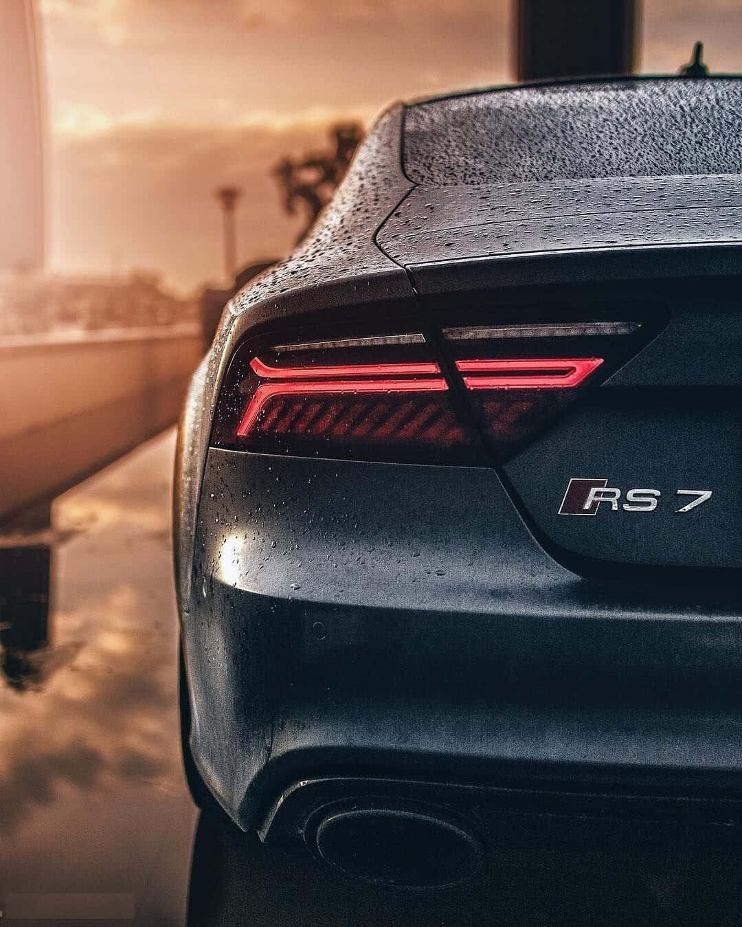 Audi S7 桌布 壁紙 — 金色夕陽城市景觀背景下，濕透的黑色奧迪RS7車尾及發光紅色尾燈特寫。