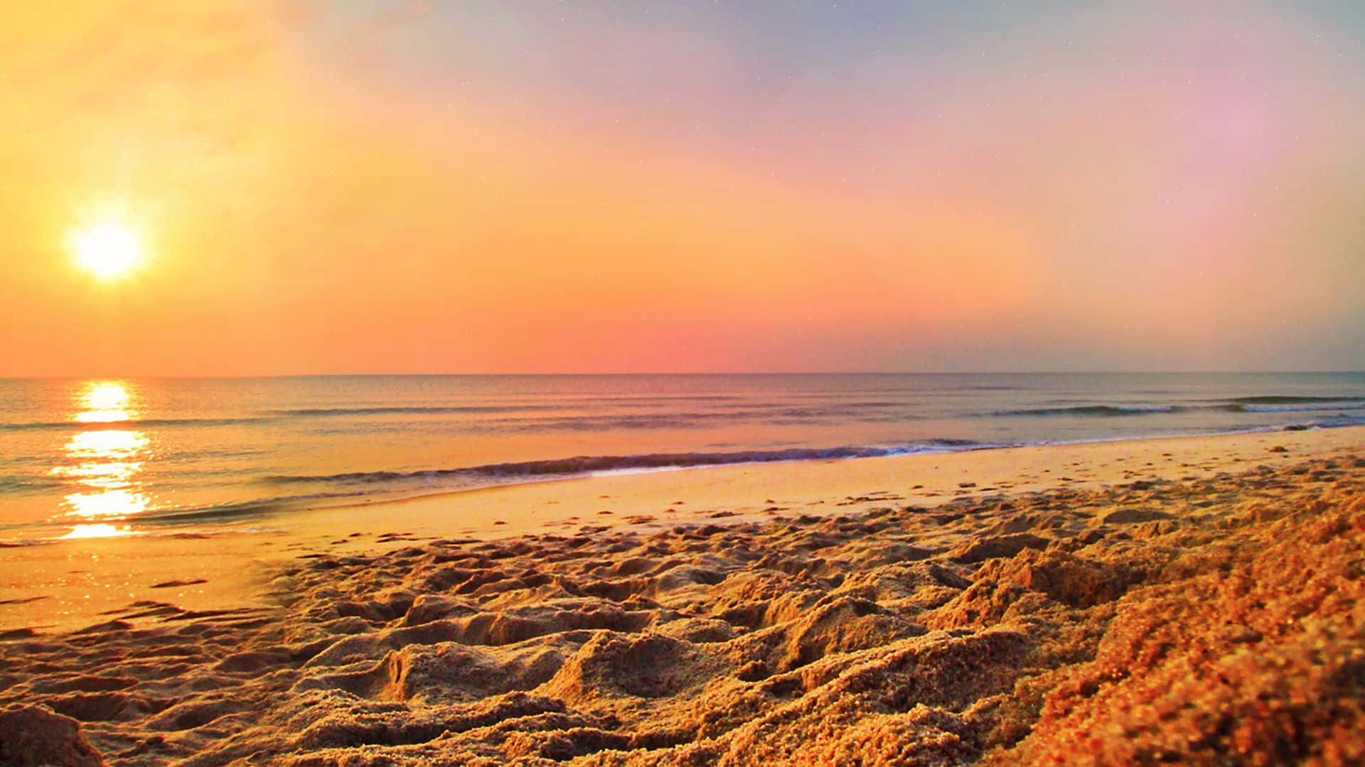 Coastal Sunset 桌布 壁紙 — 金色夕陽將溫暖光線灑在紋理沙灘上，與地平線上平靜的海浪相遇。