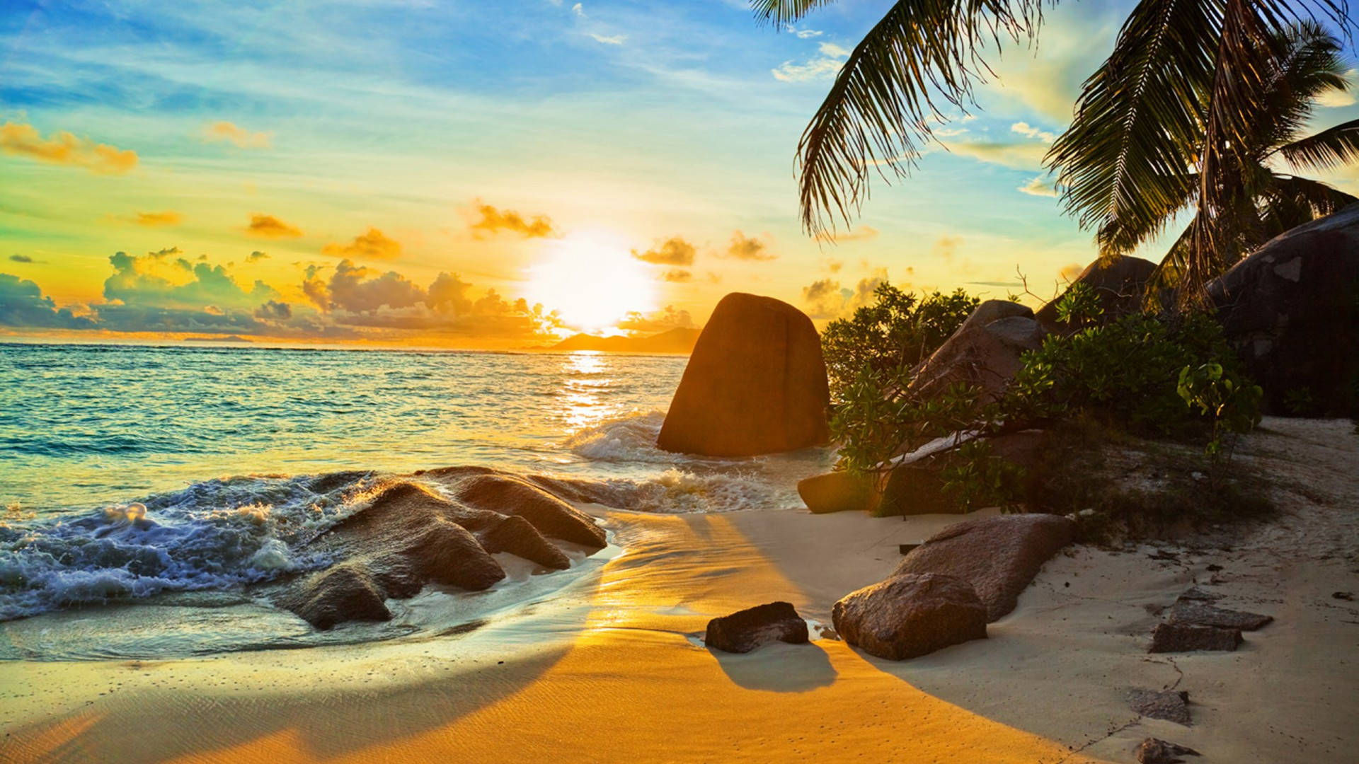 Tropical 桌布 壁紙 — 金色夕陽沐浴著熱帶海灘，棕櫚樹和碧綠的海浪拍打著光滑的岩石。