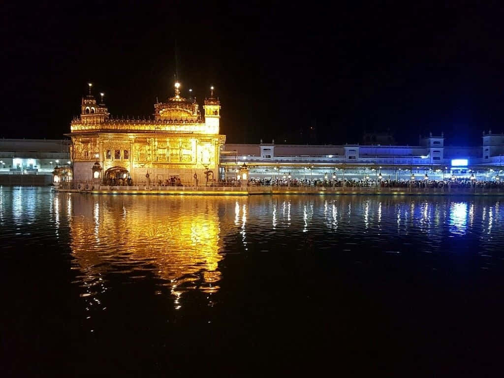 Golden Temple 桌布 壁紙 — 金色寺廟在夜晚被溫暖燈光照亮，倒映在平靜的水面上，周圍擠滿人群。