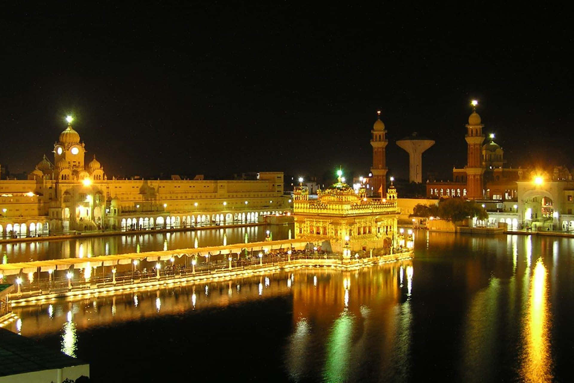 Golden Temple 桌布 壁紙 — 金色寺廟在夜晚被溫暖的燈光照亮，在黑暗的天空下平靜的水面上反射。