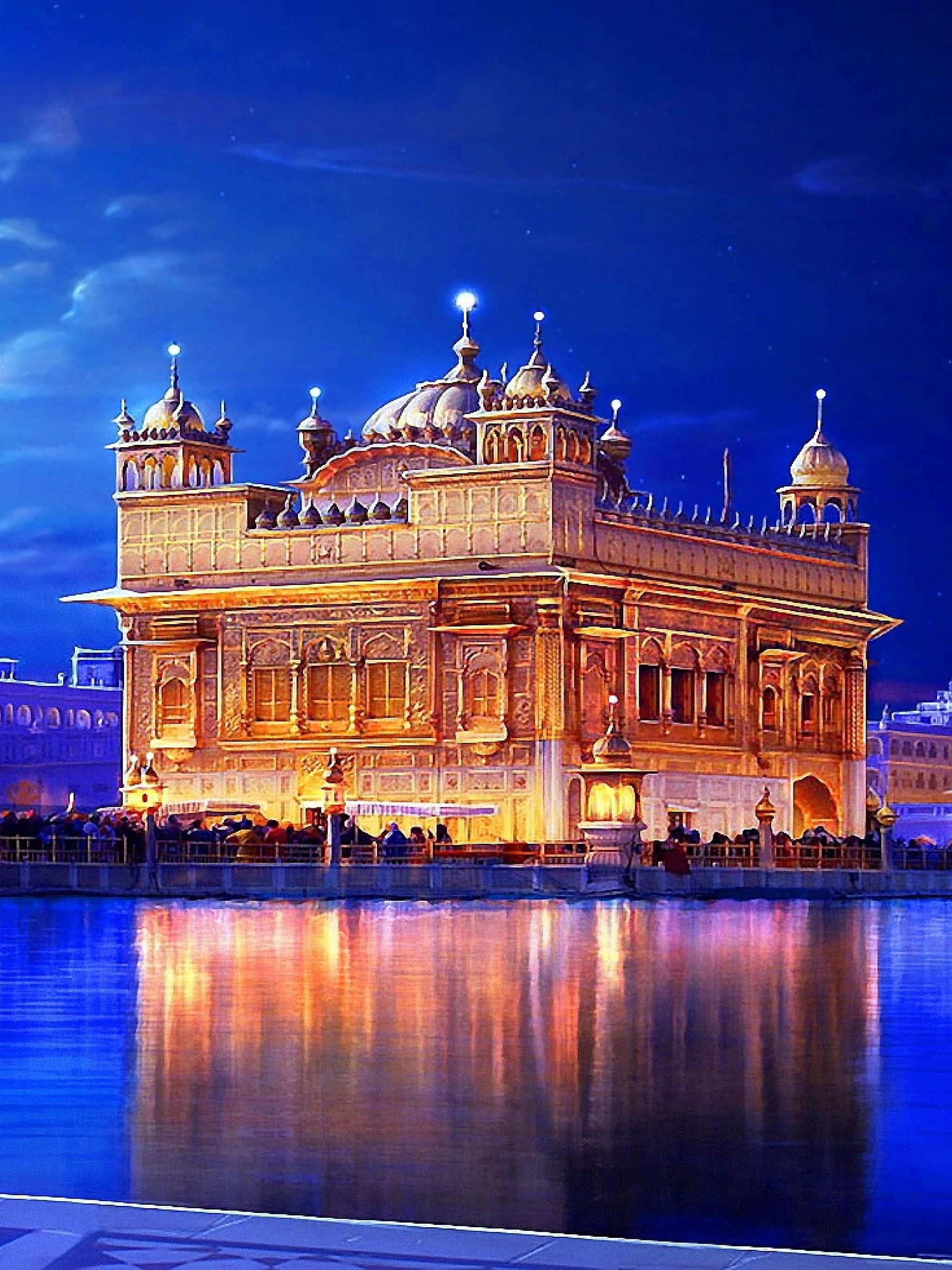 Golden Temple 桌布 壁紙 — 金色寺廟在夜晚被照亮，溫暖的燈光倒映在平靜的池塘中，背景是深藍色的天空。