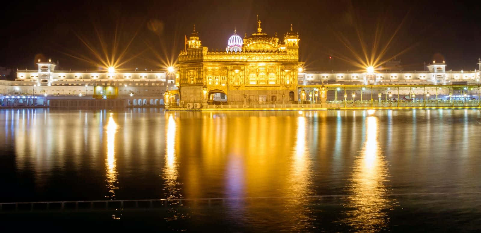 Golden Temple 桌布 壁紙 — 金色寺廟在夜晚被照亮，燦爛燈光倒映在平靜水面上，營造出寧靜的靈性氛圍。