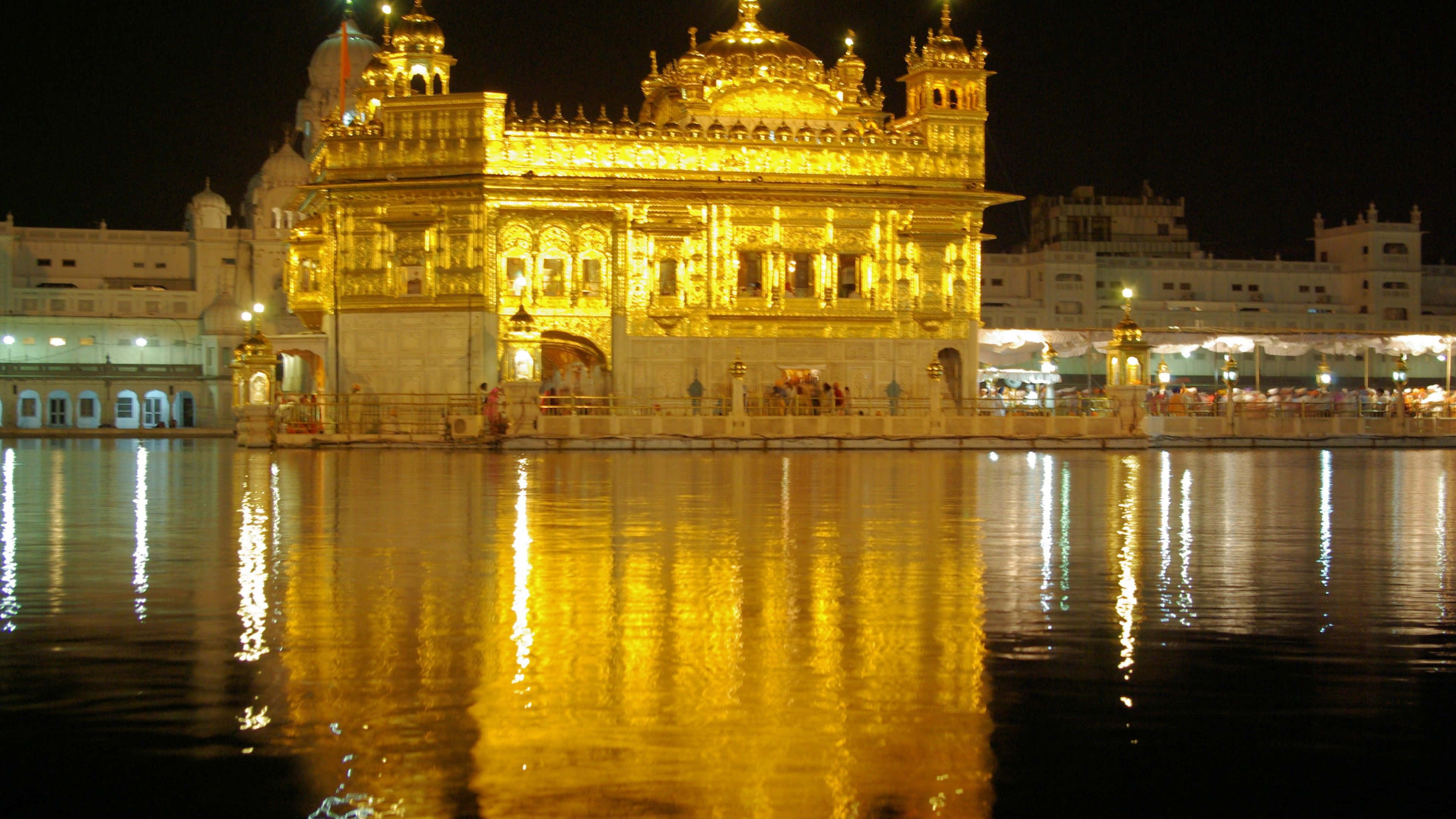 Golden Temple 桌布 壁紙 — 金色寺廟在夜燈下閃耀，平靜的水面上閃爍著舞動的倒影。