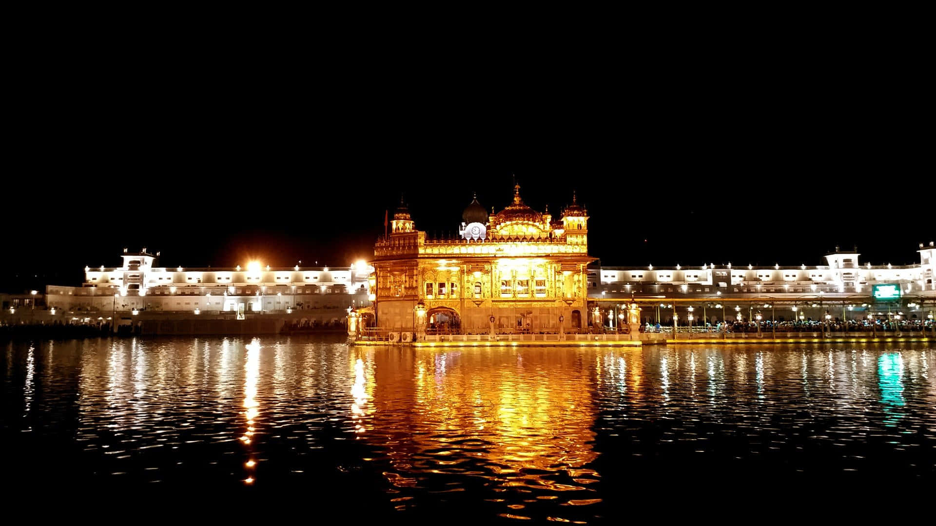 Golden Temple 桌布 壁紙 — 金色寺廟在夜空下被溫暖燈光照亮，平靜水面上倒映著光芒。