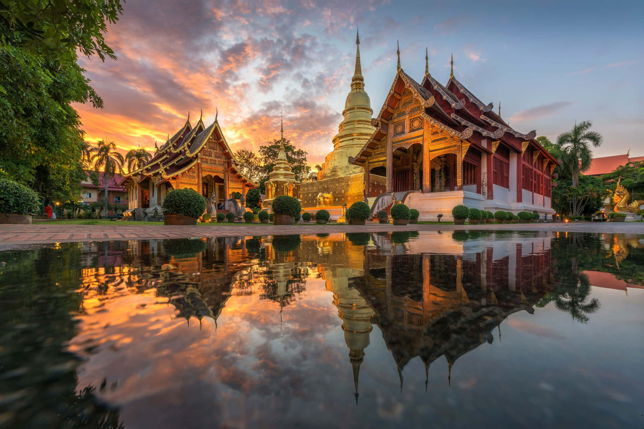 Asia 桌布 壁紙 — 金色寺廟尖頂和華麗屋頂在熾熱的日落中完美倒映在平靜的水池中。