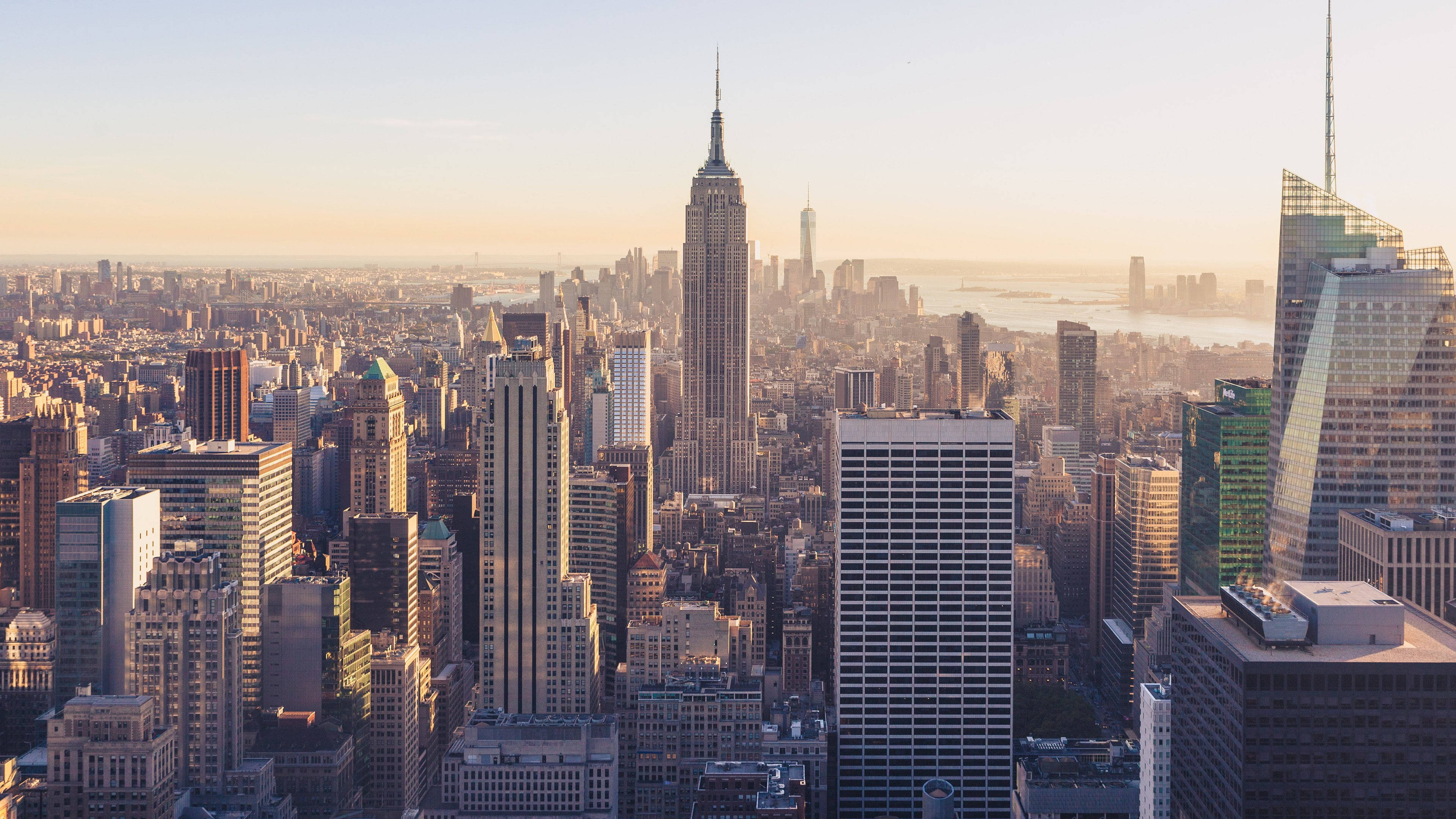 New York 桌布 壁紙 — 金色日出沐浴著紐約市標誌性的天際線，溫暖的光芒中，帝國大廈聳立在密集的城市叢林之上。